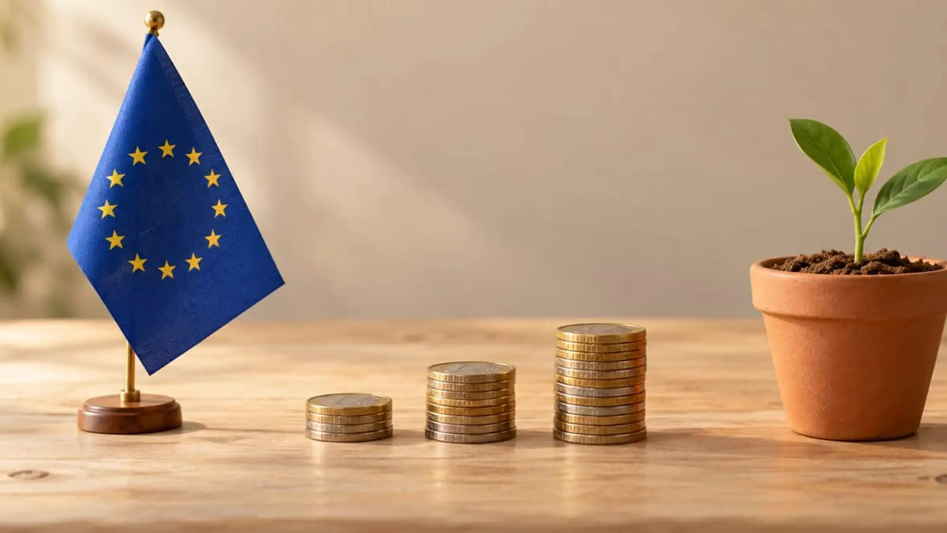 Bandera de la Unión Europea junto a tres columnas crecientes de monedas de euro y una planta joven en una maceta