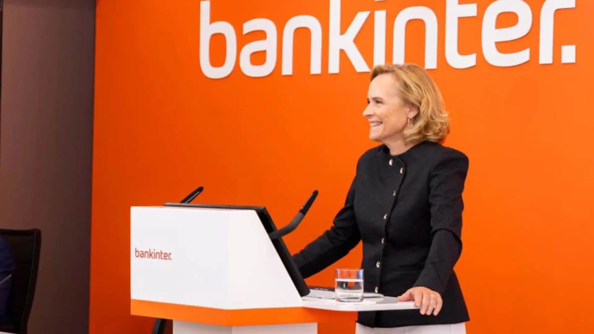 Bankinter se inunda de IA y la implanta en todo el banco para maximizar su potencial de eficiencia Gloria Ortiz, consejera delegada de Bankinter, sonriendo en atril con logo naranja.