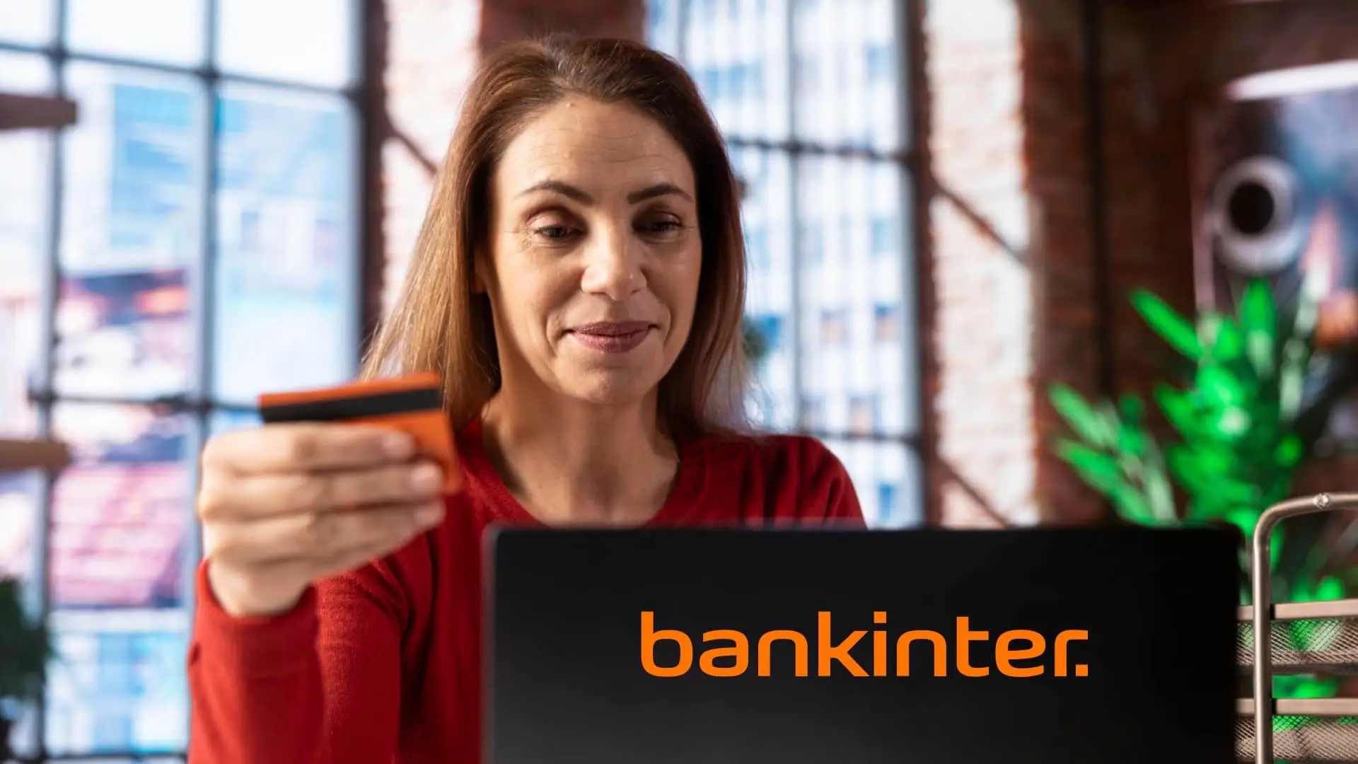 Mujer con tarjeta de Bankinter frente a un portátil realizando gestiones de banca online o pagos seguros.