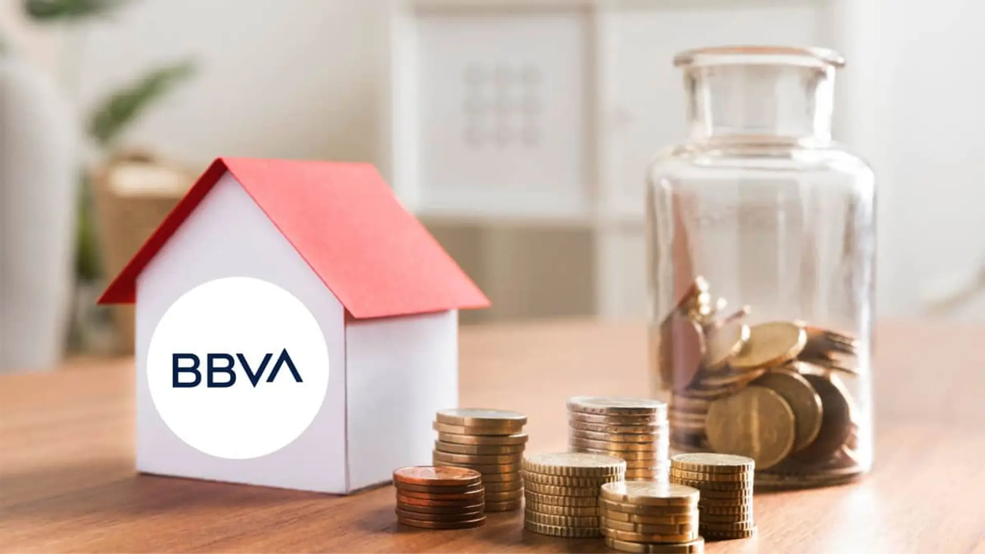 Casa en miniatura junto a monedas y una hucha, concepto de ahorro para comprar una vivienda con una hipoteca BBVA.