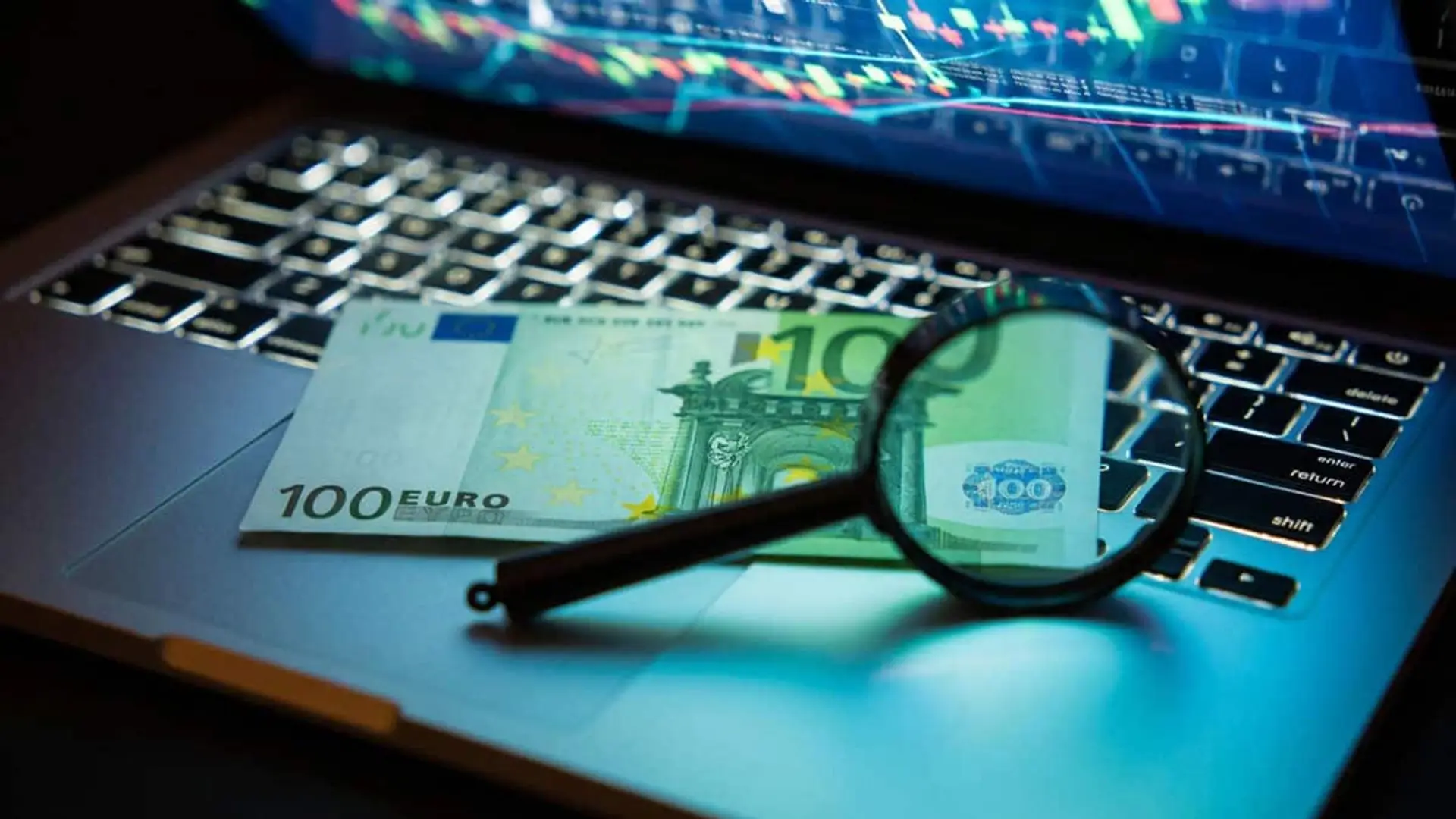 Por qué Santander, BBVA y CaixaBank han unido sus sistemas para detectar fraudes que ninguno vería solo Billete de 100 euros y una lupa sobre el teclado de un portátil con gráficos financieros al fondo