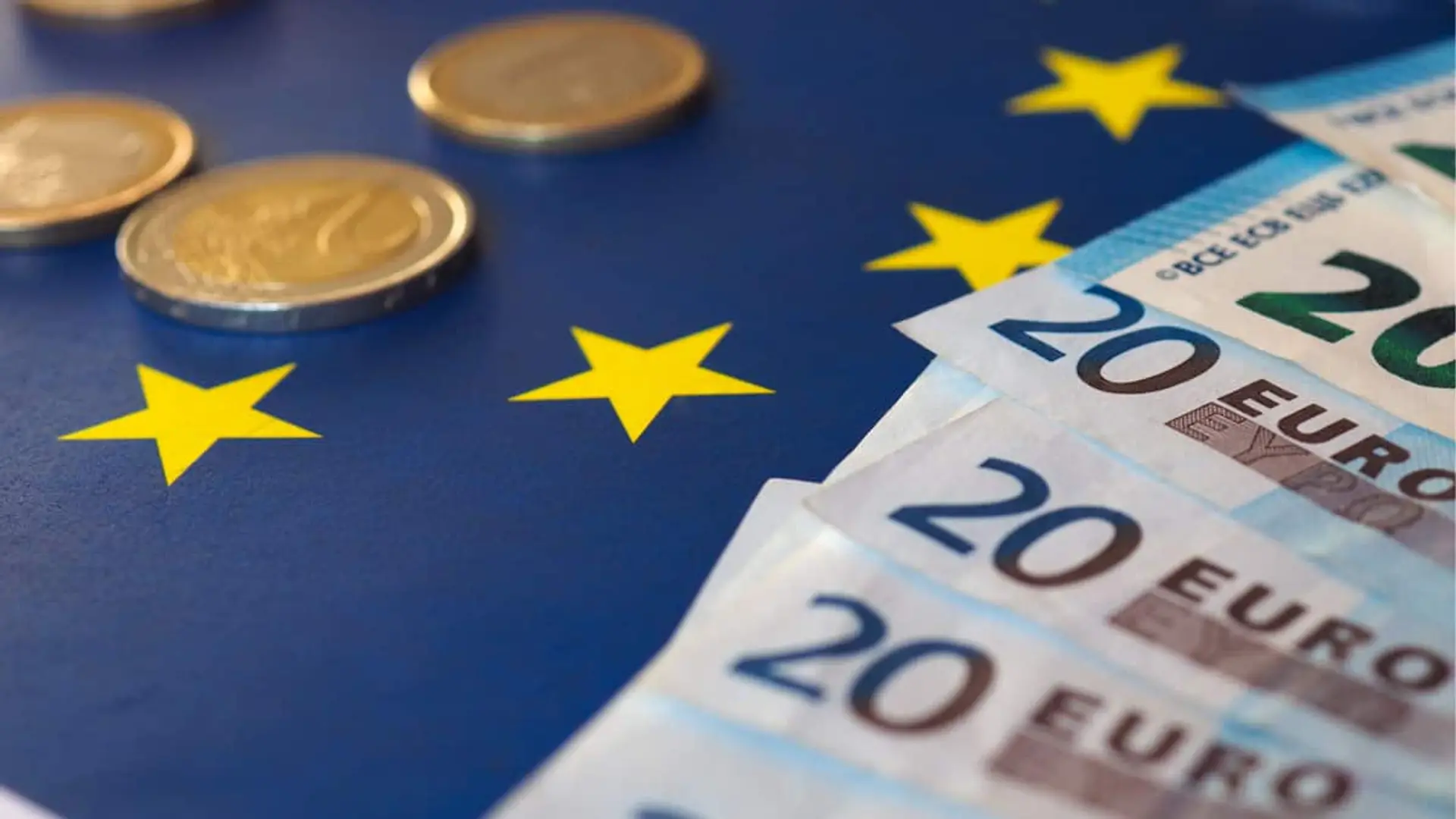 Monedas de 2 euros y billetes de 20 eutos sobre una bandera de la UE.
