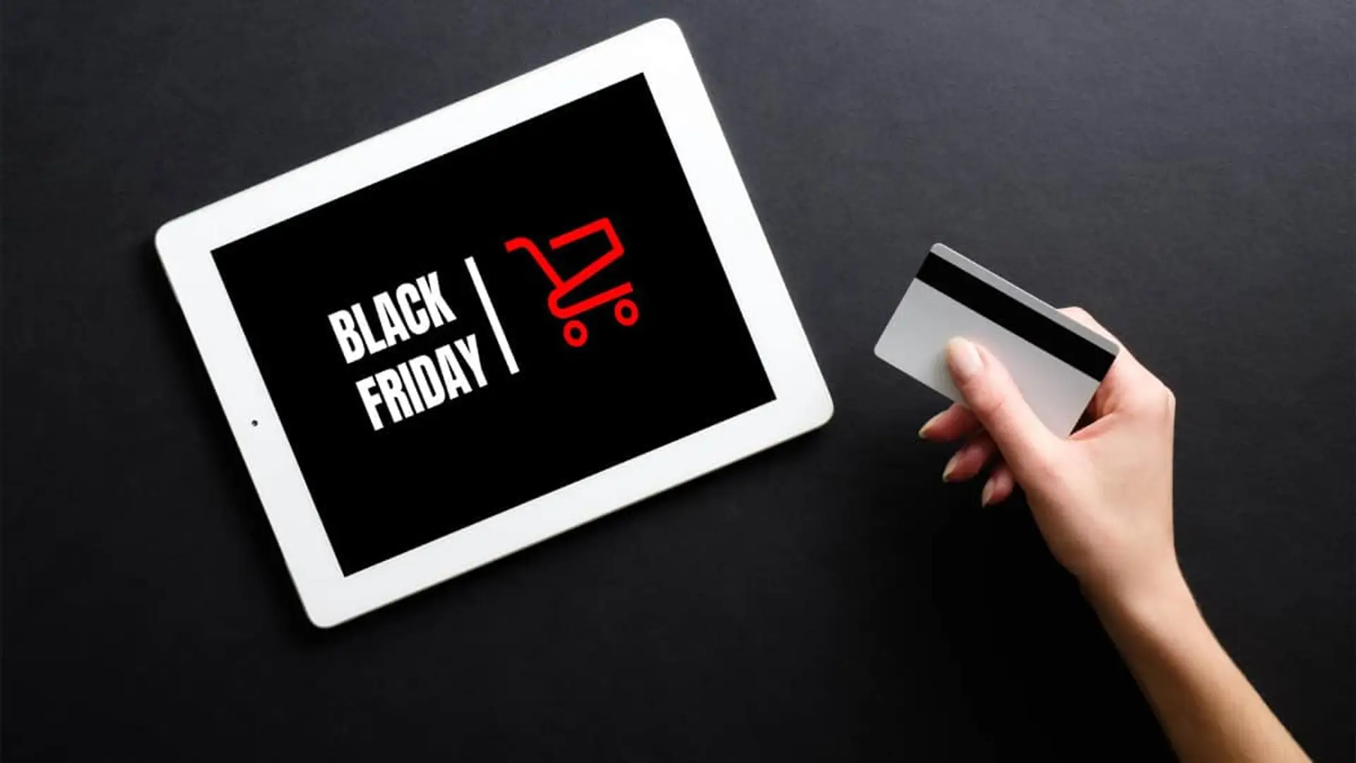 Mano con tarjeta de crédito pagando oferta de Black Friday en pantalla de tablet sobre fondo negro.
