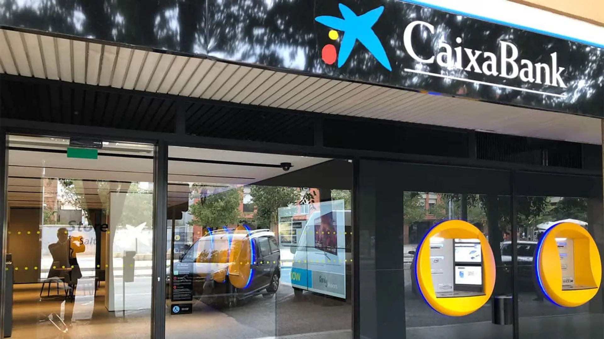 Fachada de una oficina de CaixaBank con cajeros automáticos visibles desde la calle.