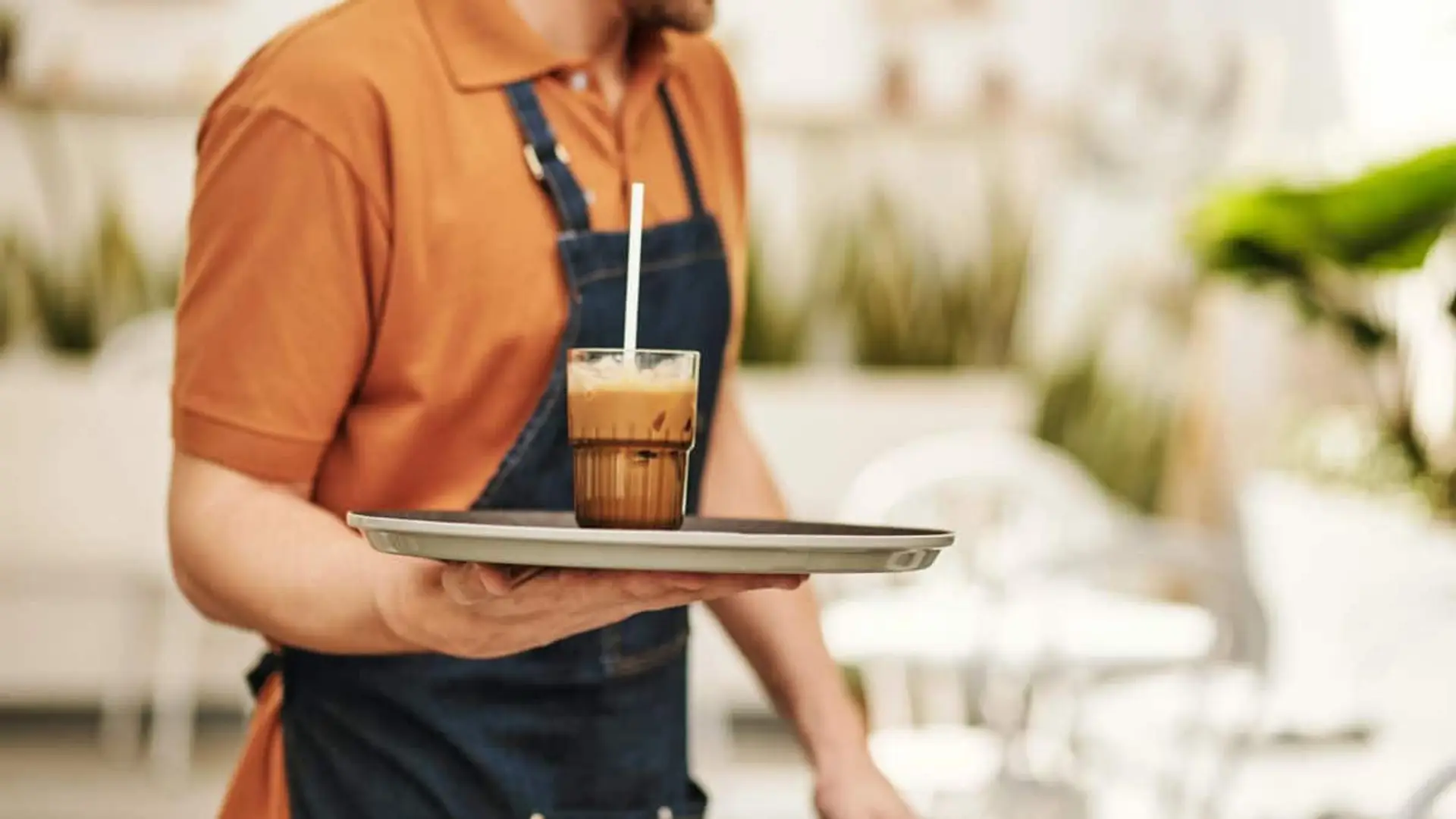 Camarero con delantal sosteniendo una bandeja con un vaso de café frío