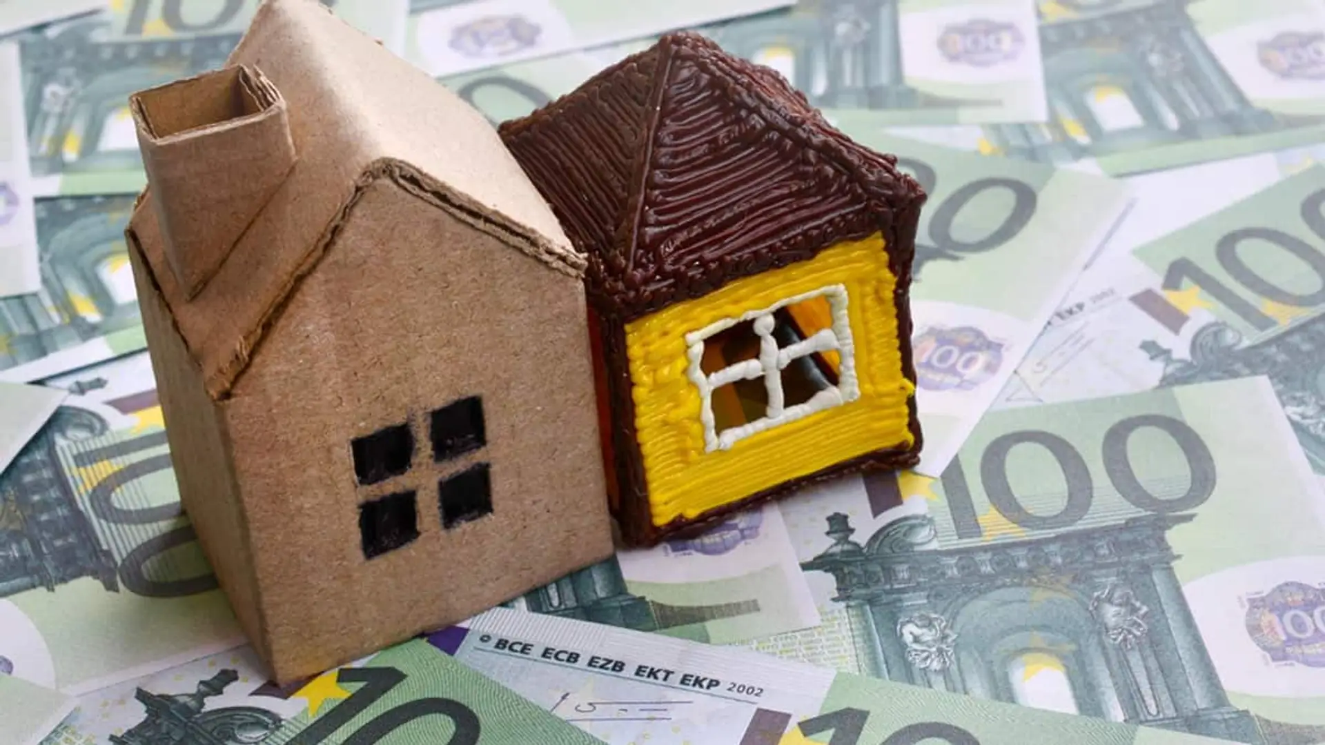 Dos casas en miniatura colocadas sobre billetes de euro.
