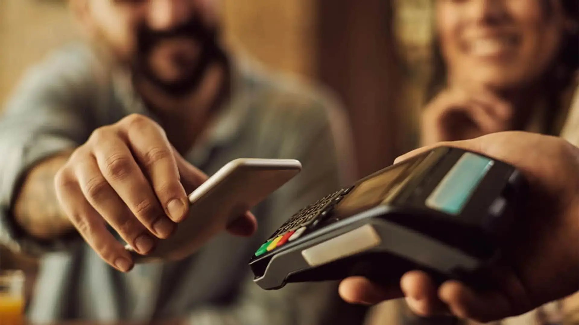 Primer plano de cliente pagando contactless con móvil tecnología NFC en datáfono.