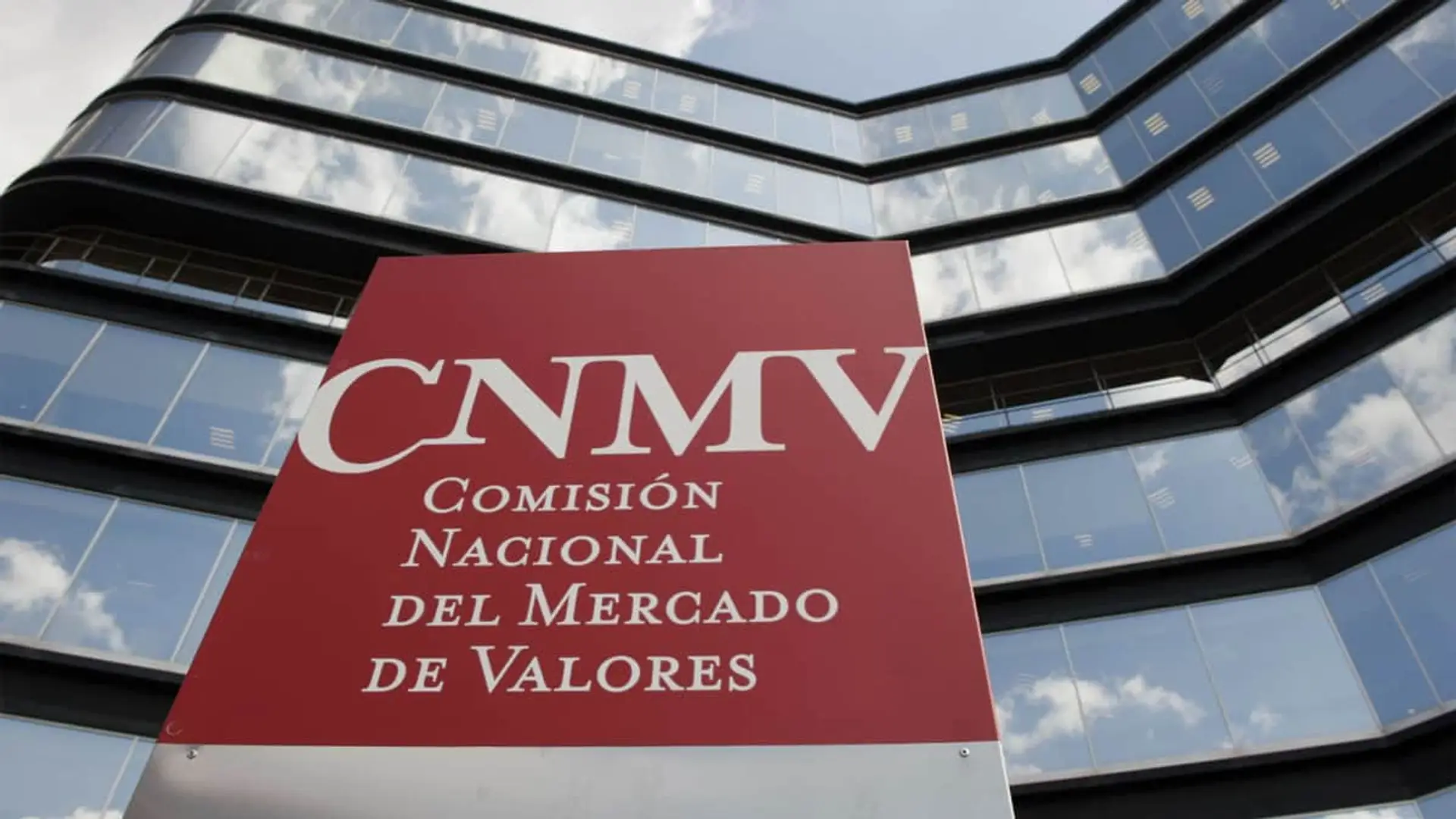 Cartel rojo con logotipo de la CNMV frente a la fachada de cristal de su sede corporativa.