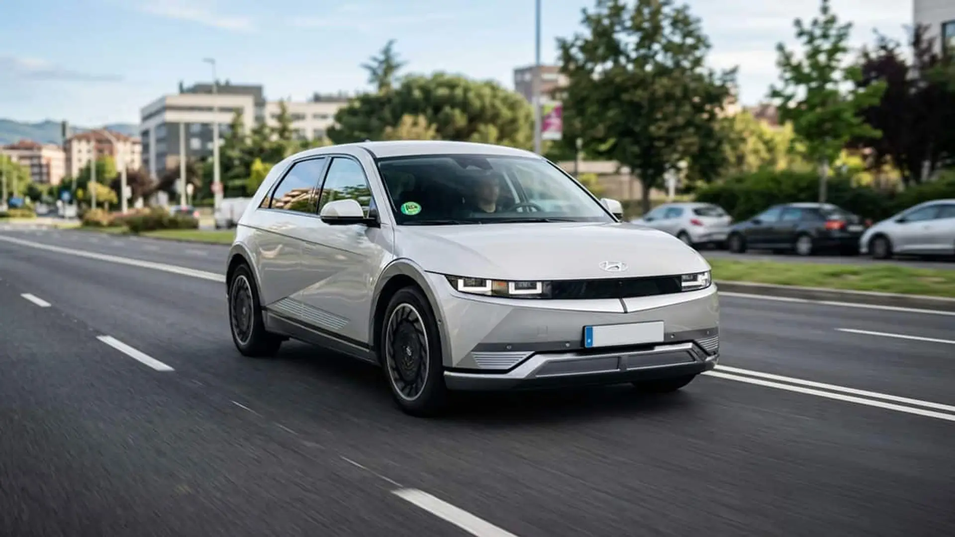 Coche eléctrico circulando por una avenida urbana con edificios y árboles al fondo