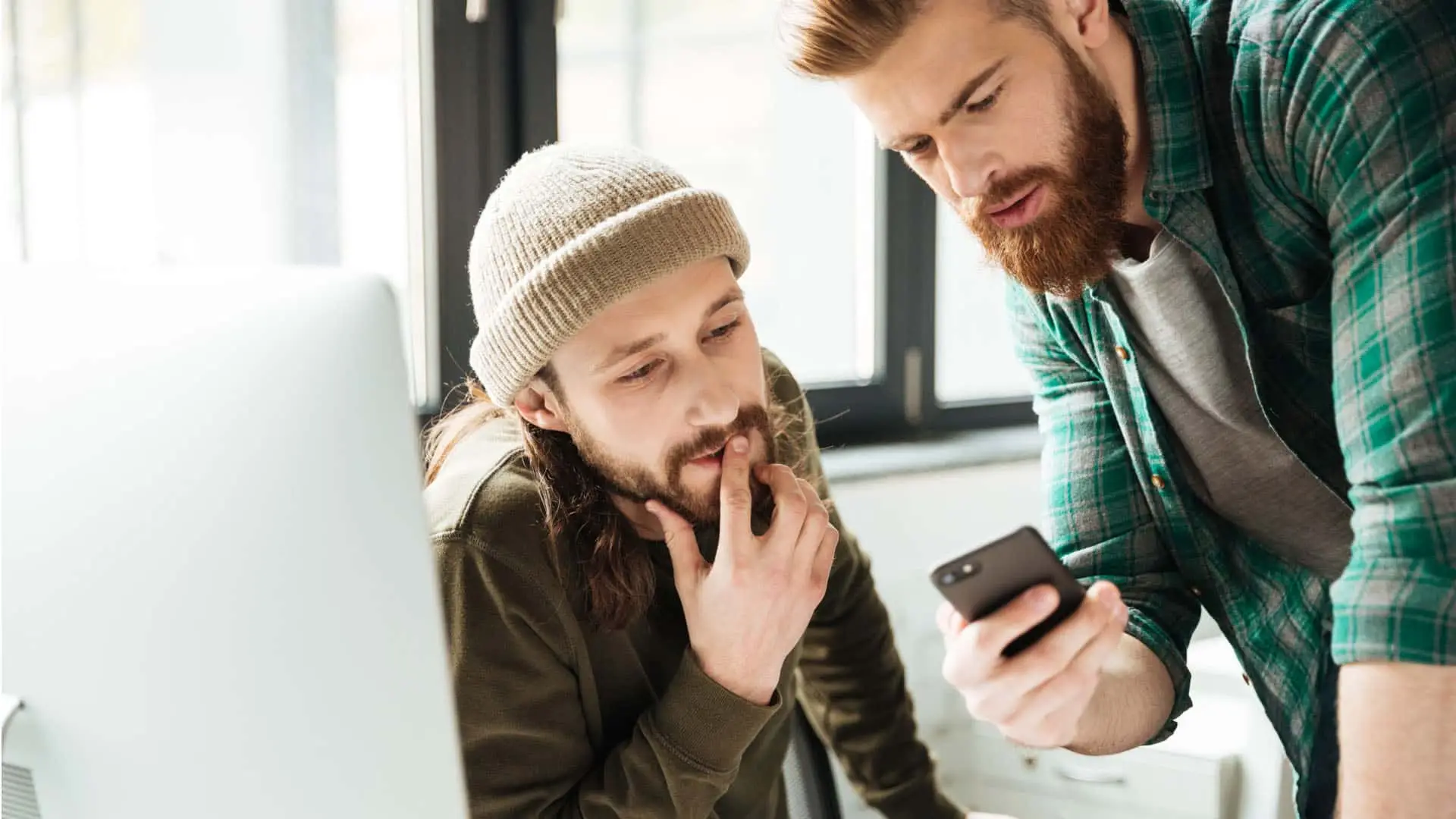 Dos compañeros de trabajo colaborando en un proyecto en la oficina. Uno comparte una idea desde su móvil con su colega.