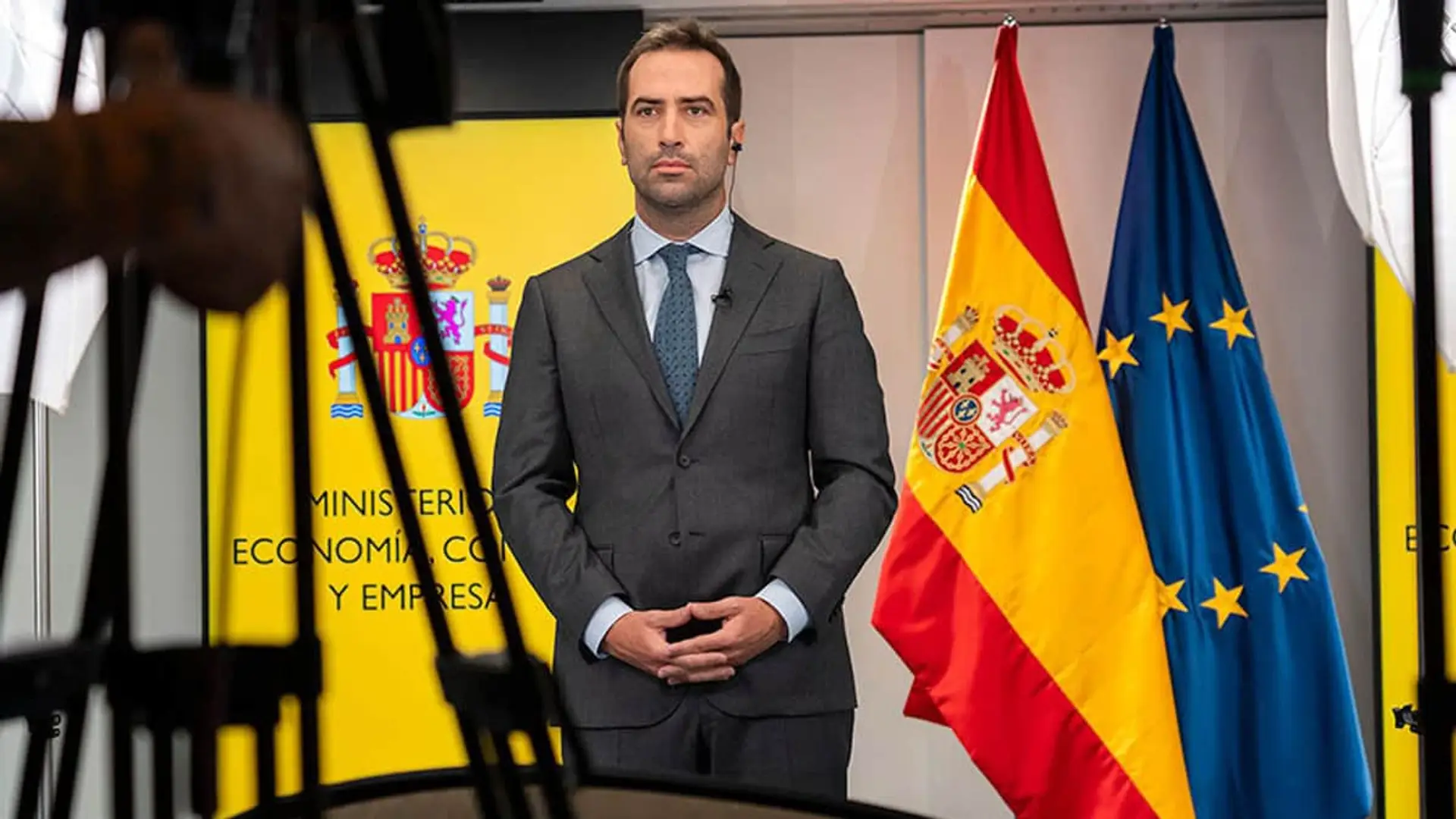 Carlos Cuerpo Ministro de Economía, Comercio y Empresa en rueda de prensa ante banderas de España y UE.