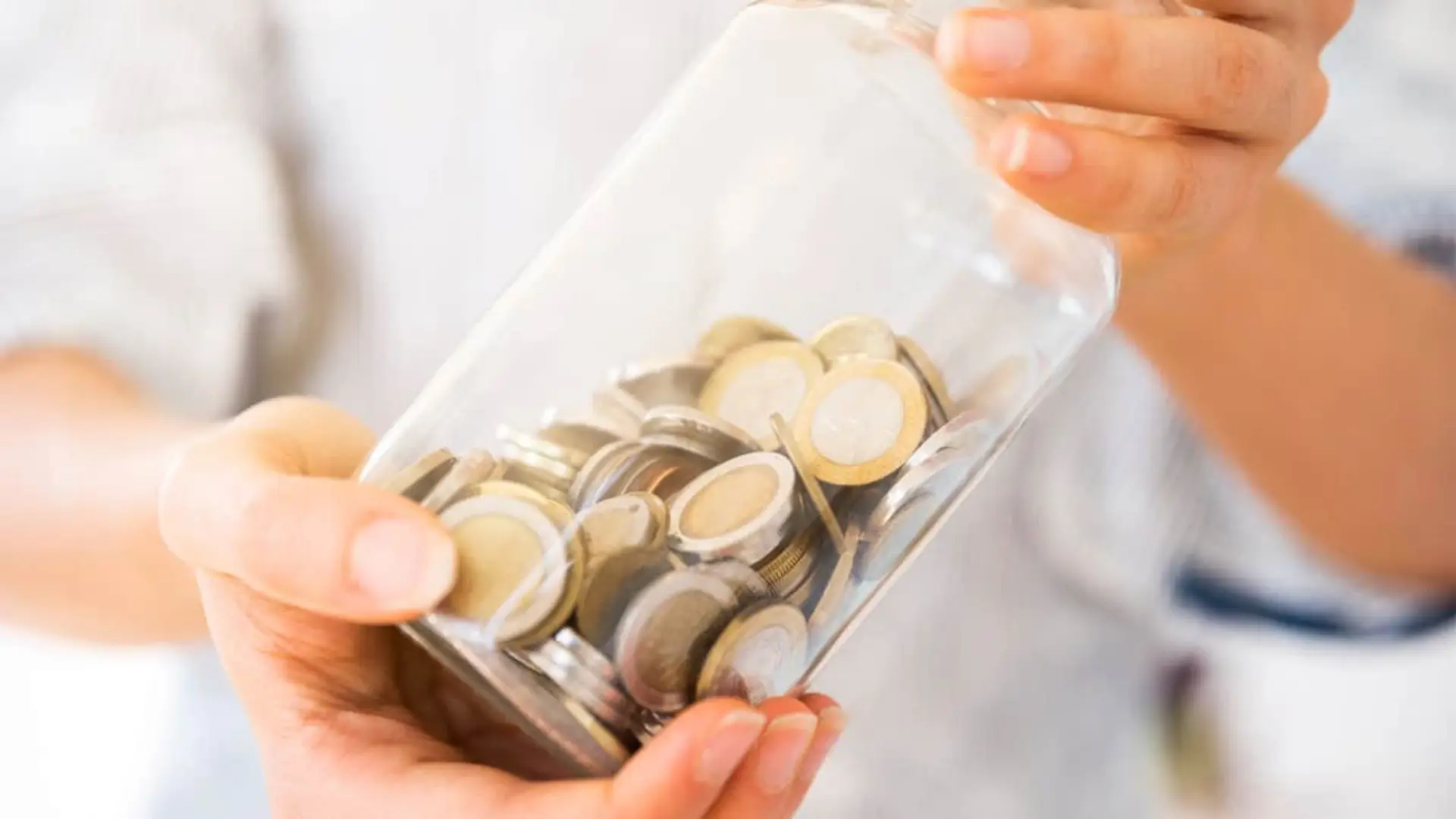 Así es el depósito al 3,69% TAE a 12 meses para rentabilizar tus ahorros Persona sosteniendo un bote de cristal lleno de monedas, una metáfora del ahorro y la rentabilidad de los depósitos.