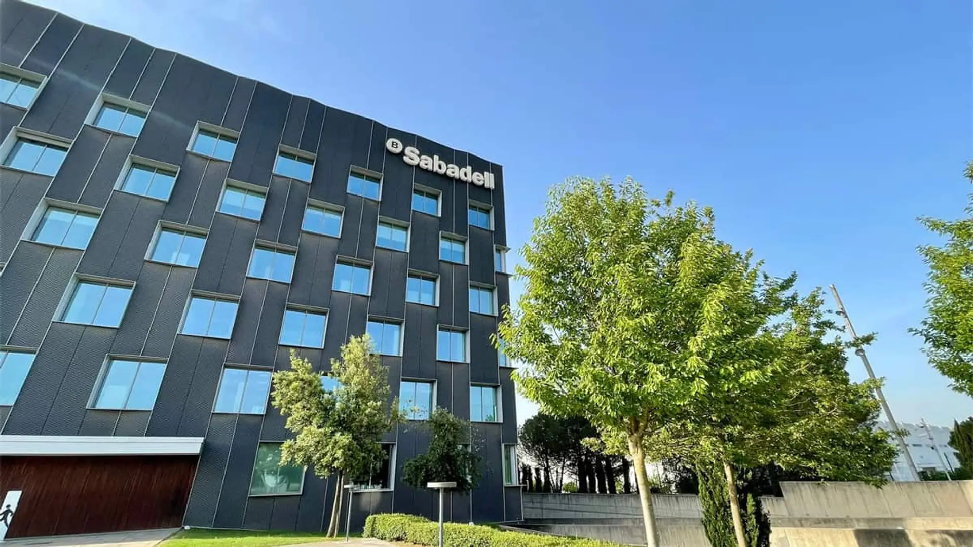 Visión desde el exterior de la sede del Banco Sabadell, con zona verde con árboles.