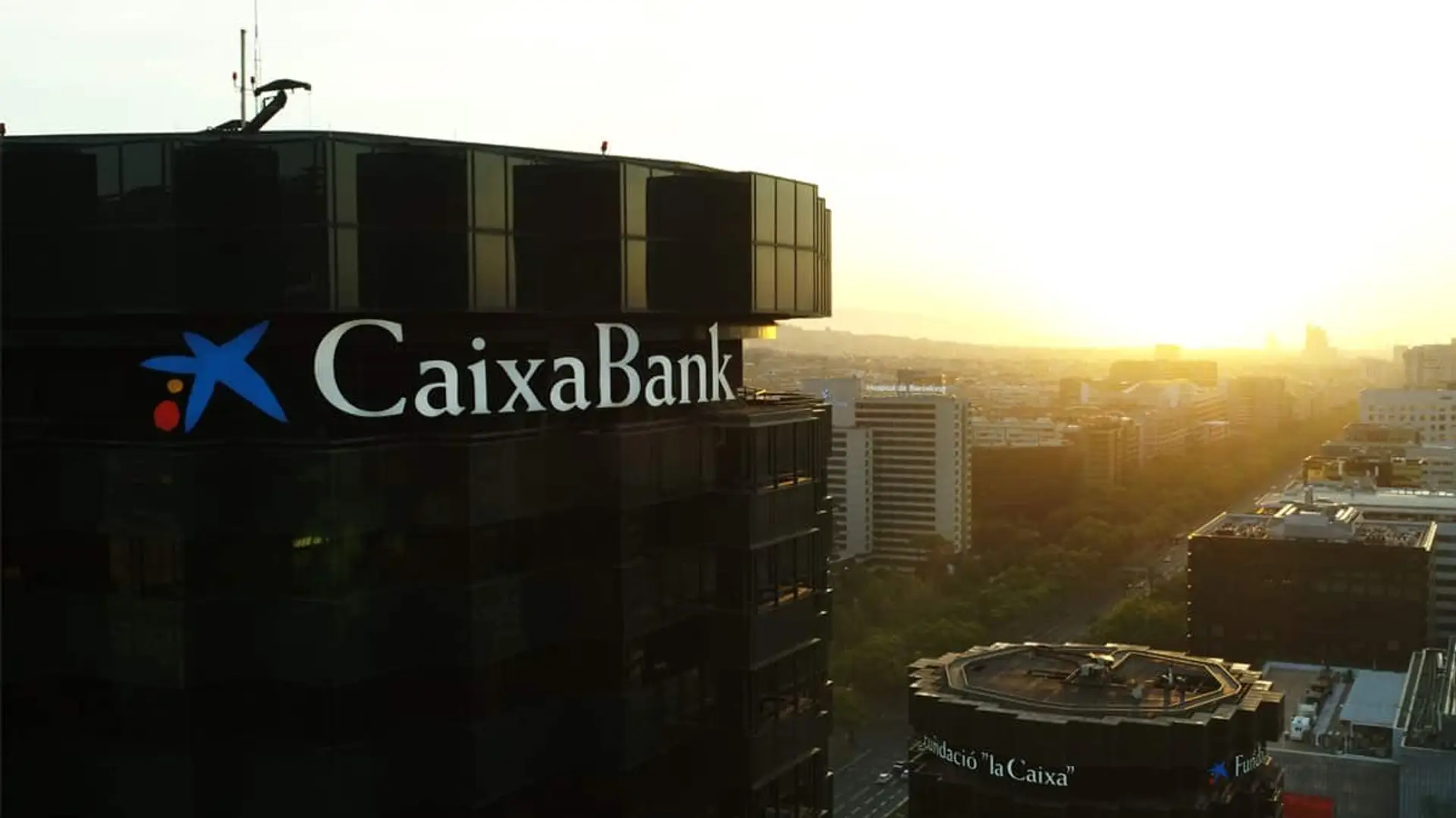 Edificio de CaixaBank con el logotipo en la fachada y la ciudad al fondo al atardecer