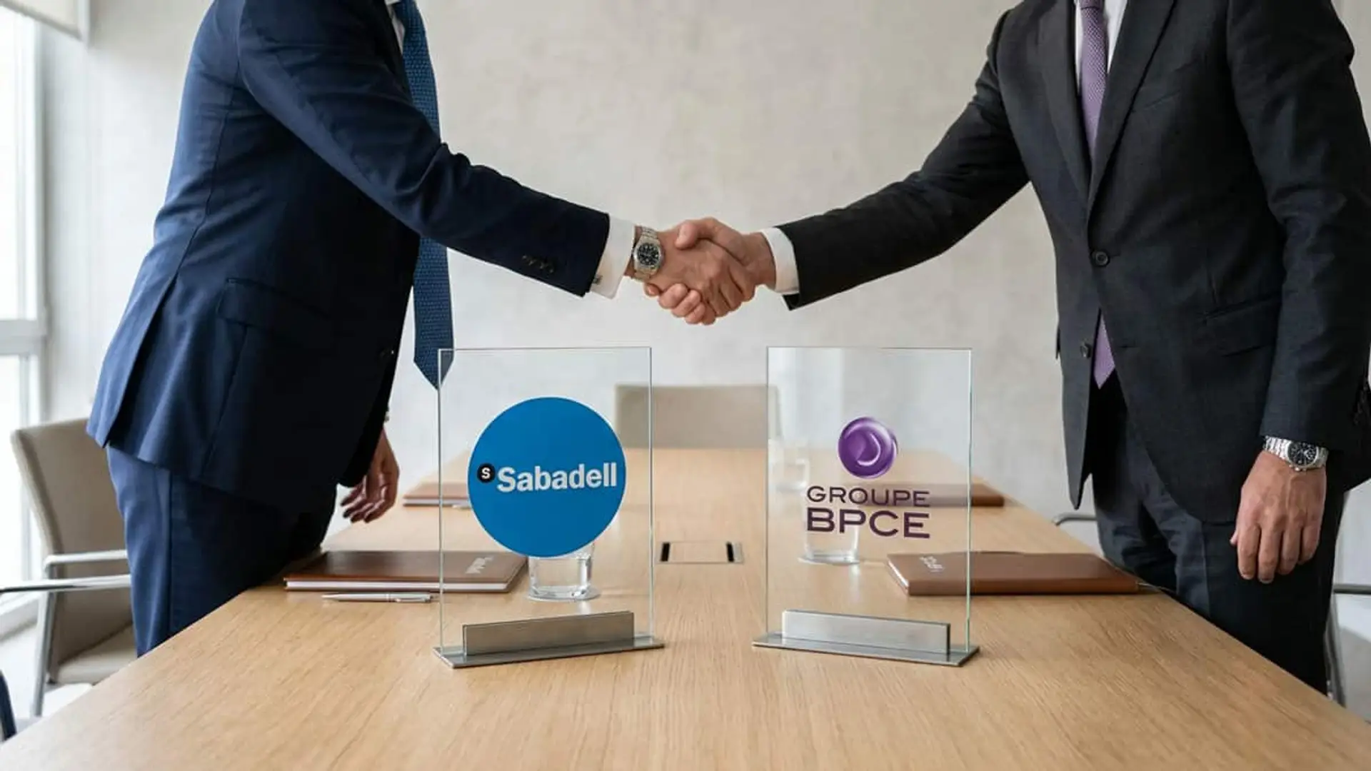 Dos ejecutivos estrechándose la mano junto a los logotipos de Banco Sabadell y Groupe BPCE