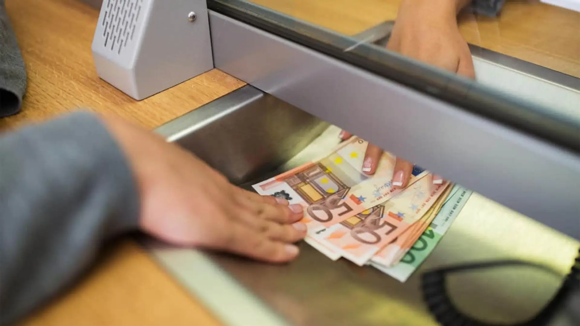 Cliente recibiendo efectivo con billetes de euro en ventanilla bancaria.