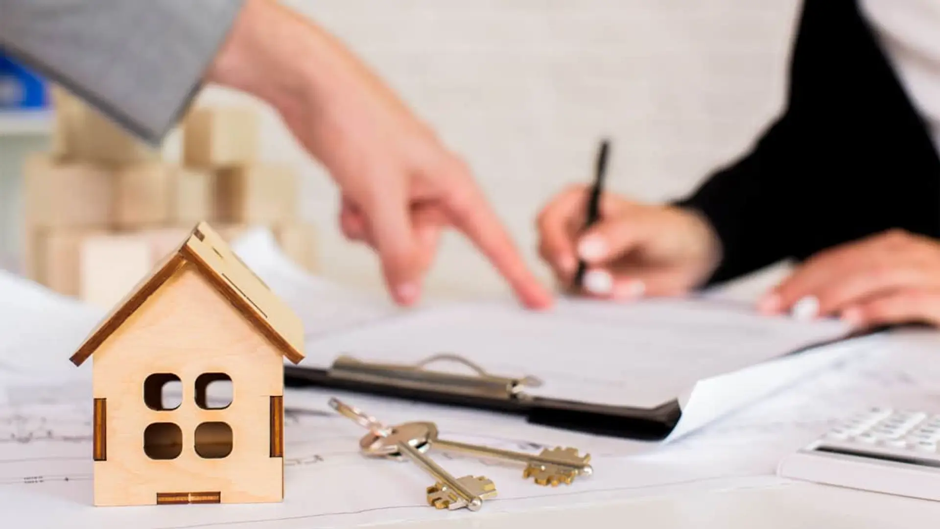 Persona firmando un contrato de hipoteca para comprar una casa. En el escritorio, las llaves y una maqueta de la vivienda.
