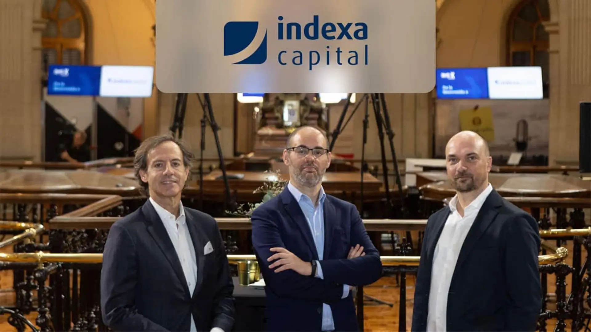 Los socios fundadores de Indexa Capital posan para una foto en la Bolsa y se ve el logotipo azul de la compañía sobreimpresionado.