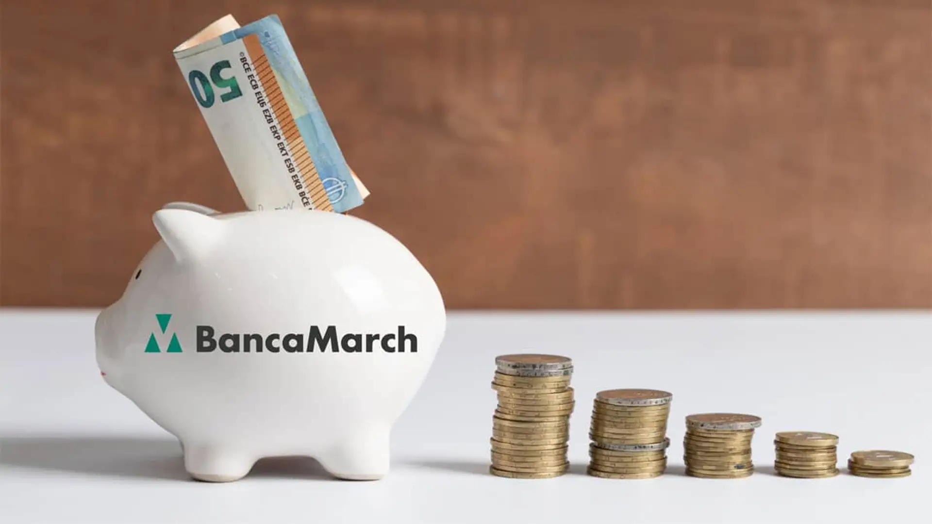 2,50% TAE a 12 meses: el nuevo depósito de Banca March para ahorradores con más de 30.000 euros Hucha de Banca March con un billete de cincuenta euros y pilas de monedas para representar el ahorro y la inversión financiera.