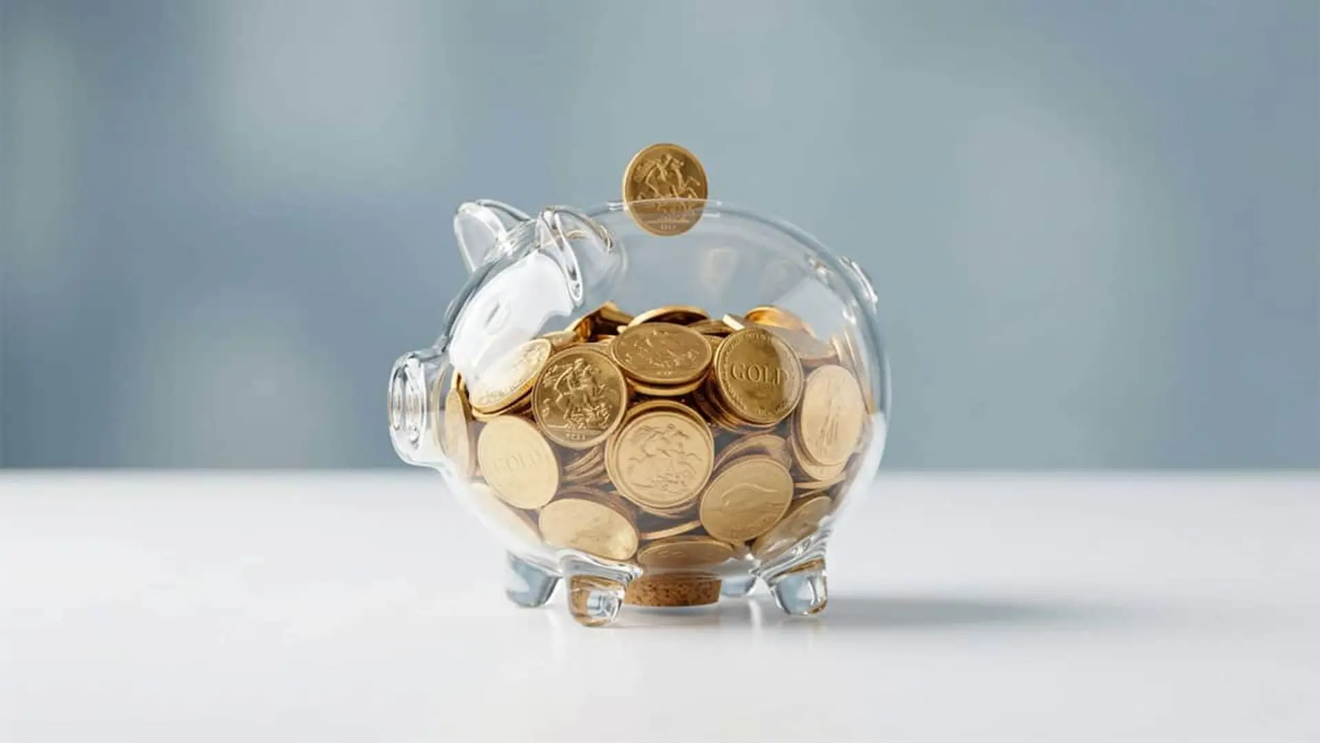 Qué descuentos puedes conseguir solo por tener cuenta en un banco digital: viajes, ocio y cashback Hucha de cristal llena de monedas doradas, símbolo de ahorro, inversión y crecimiento financiero.