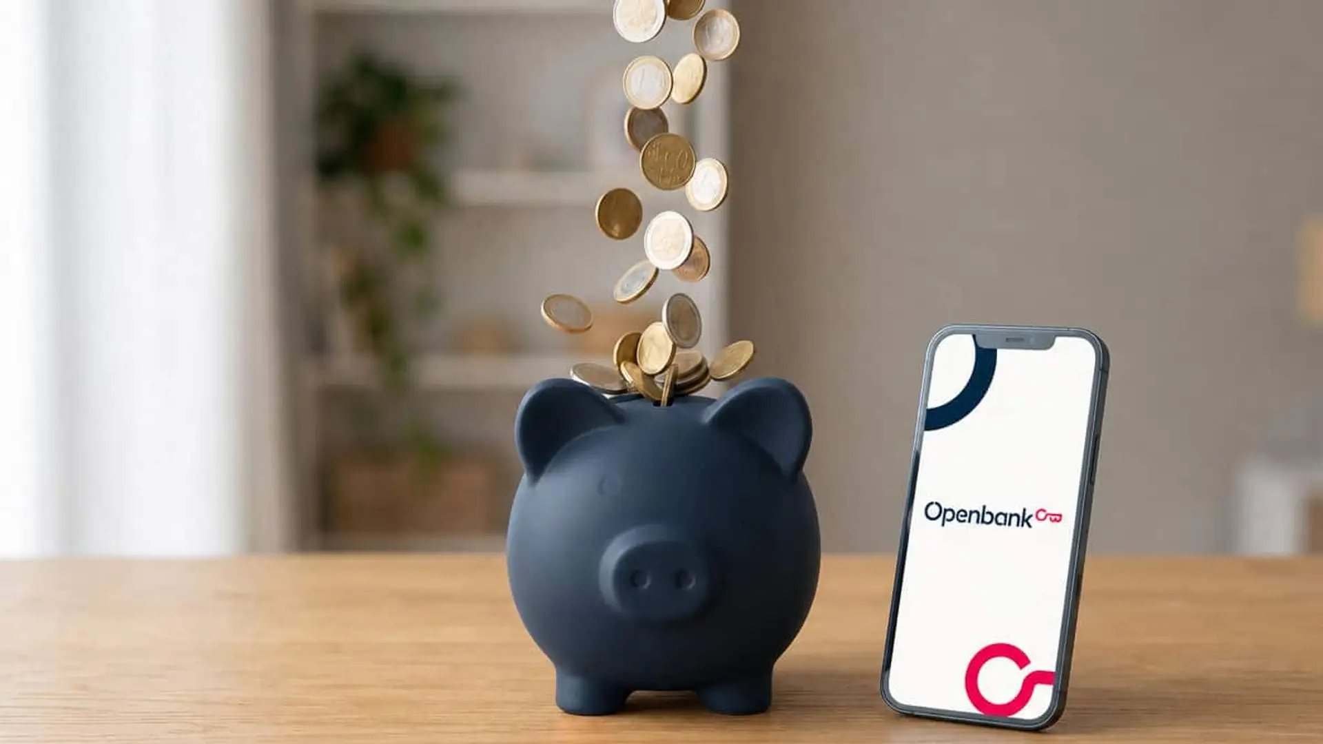 Openbank te paga el 2,75% TAE por tus ahorros: lo que ganas con 10.000€ en un año Hucha con monedas de euro cayendo en su interior junto a un teléfono móvil con el logotipo de Openbank