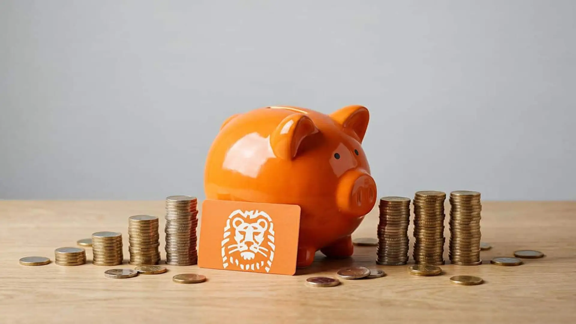 ING ampliará su oferta de pensiones con 8 fondos: uno para jóvenes y tres para el País Vasco Hucha naranja junto a una tarjeta de ING y varias pilas de monedas sobre una mesa