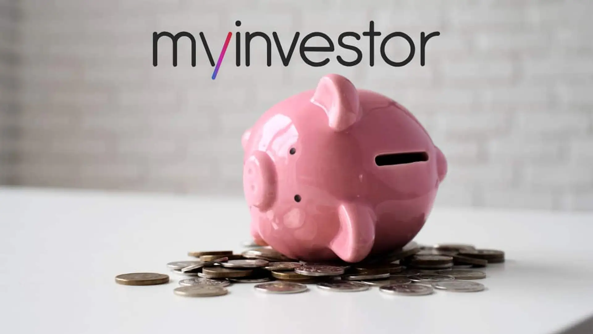 Hucha rosa sobre una mesa con monedas y el logotipo de MyInvestor al fondo