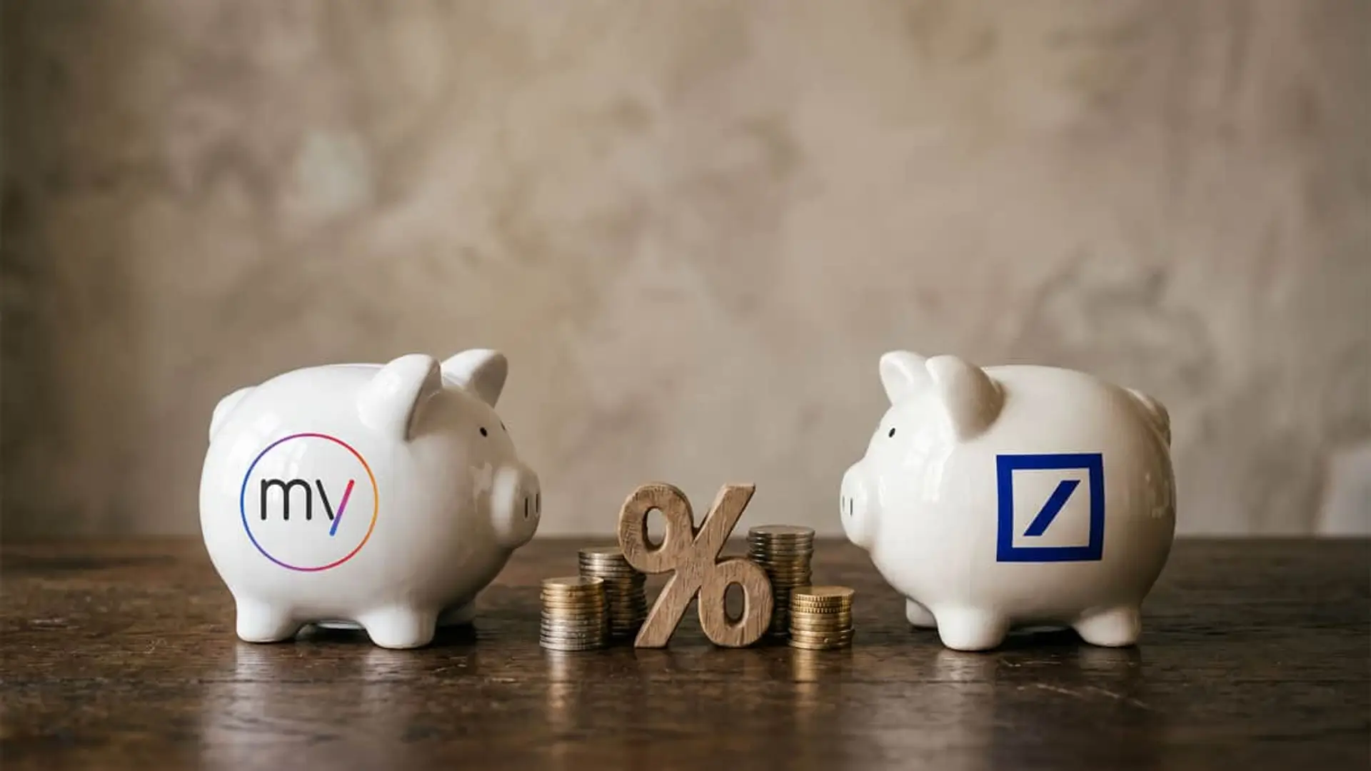 Huchas de MyInvestor y Deutsche Bank junto a monedas y un símbolo de porcentaje sobre una mesa de madera.