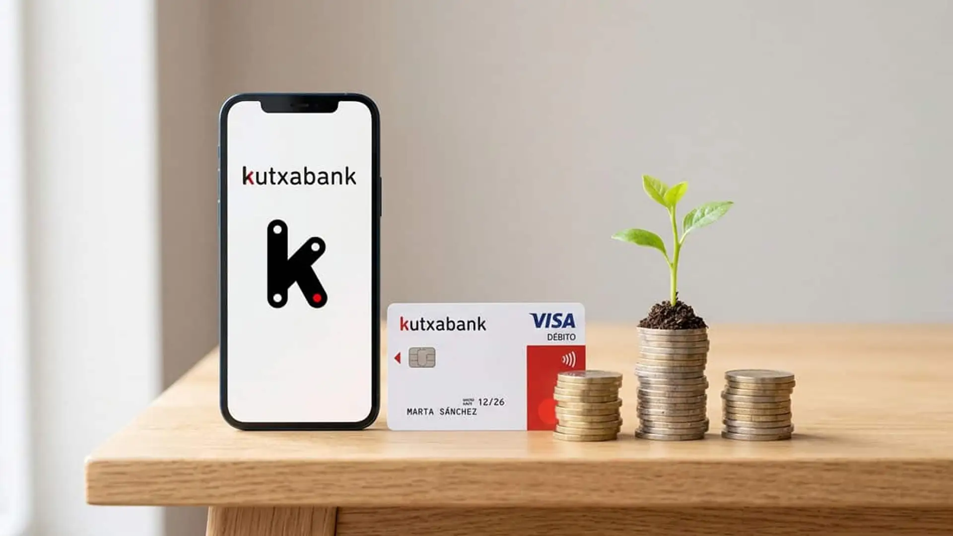 Kutxabank sube al 3,10% TAE su cuenta remunerada: así queda frente a Revolut, Trade Republic o B100 Móvil con el logotipo de Kutxabank junto a una tarjeta Visa y varias pilas de monedas, una de ellas con una planta