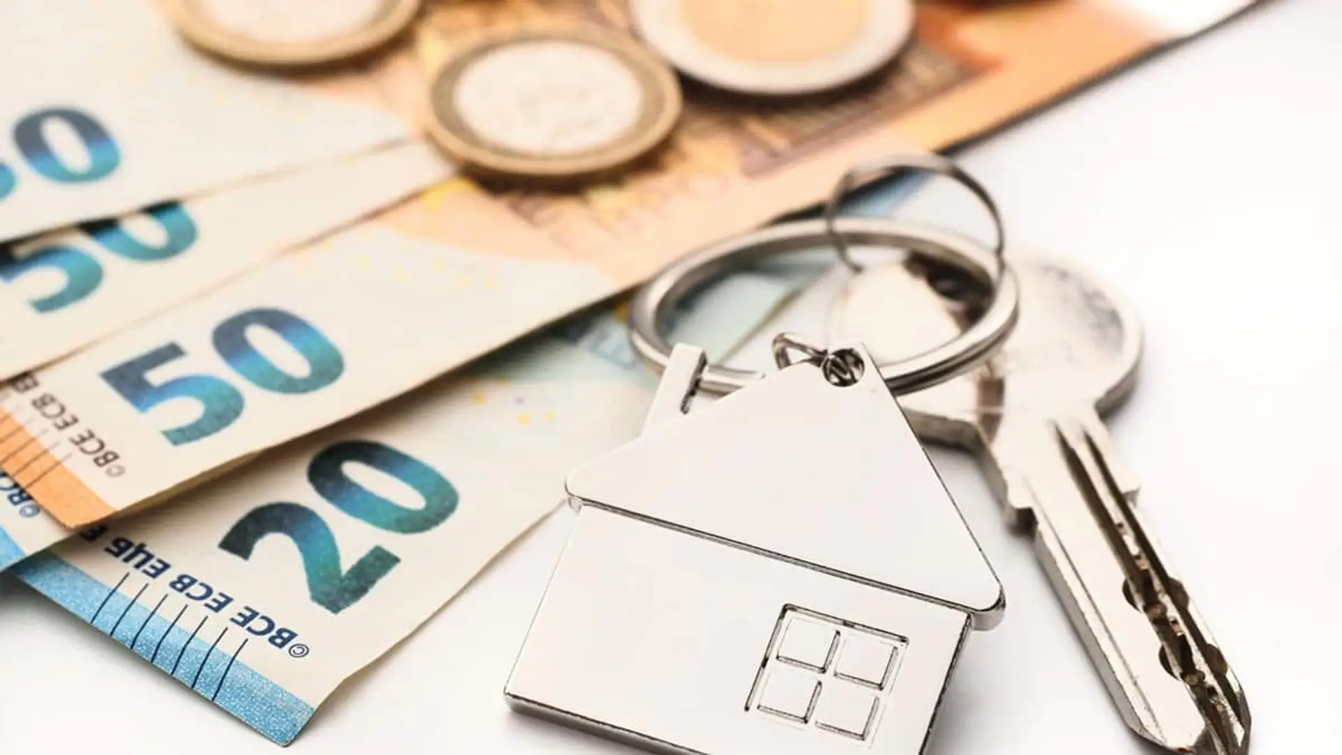 Llaves con llavero en forma de casa sobre billetes y monedas de euro.
