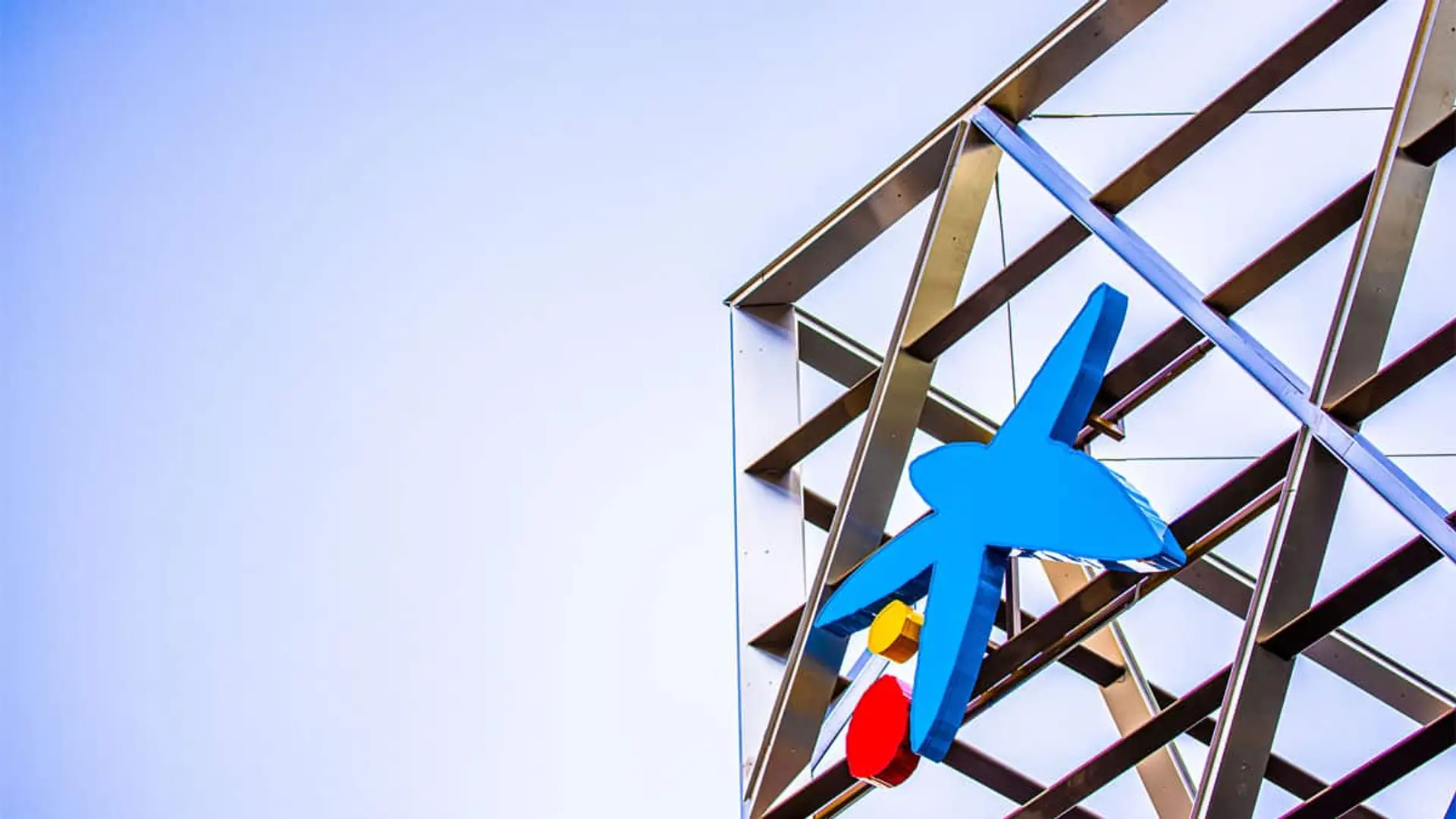 Logo de CaixaBank en la fachada de un edificio corporativo con estructura metálica y cielo despejado.
