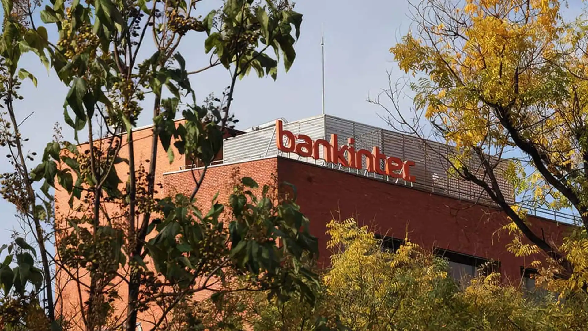 Invertir en ETF con Bankinter será más fácil: elimina la comisión de compra de estos fondos Fachada de un edificio de ladrillo con el logotipo naranja de Bankinter, entre árboles.