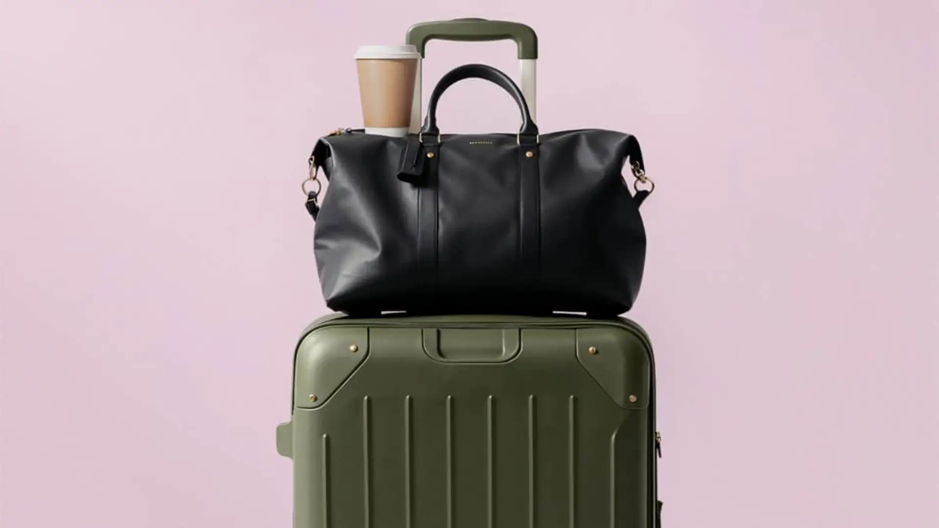 Viaja ahora y paga después: ALSA y Klarna lanzan el pago en tres plazos sin intereses para autobuses por toda España Maleta de cabina verde oliva con bolsa de viaje negra y café para llevar encima, sobre fondo rosa