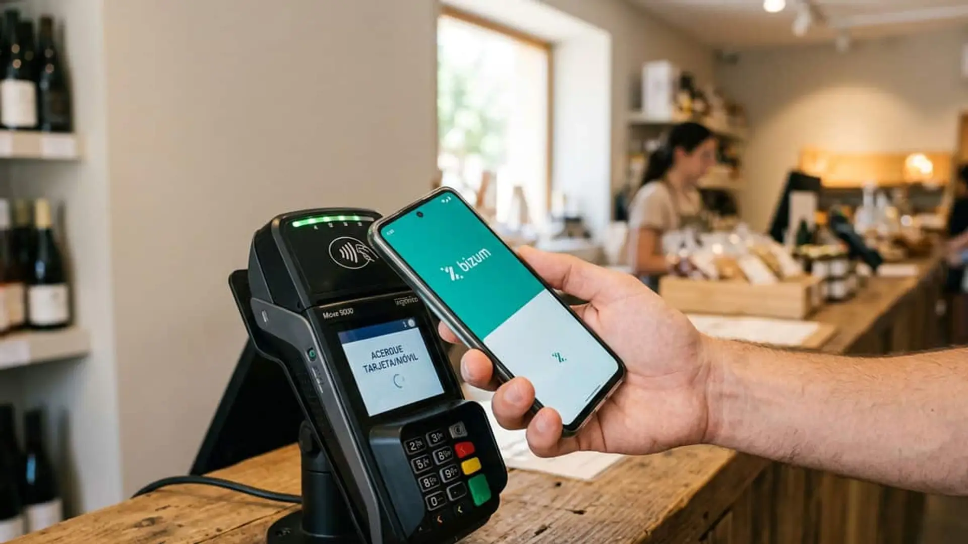 Mano acercando un móvil con Bizum a un terminal de pago en el mostrador de una tienda