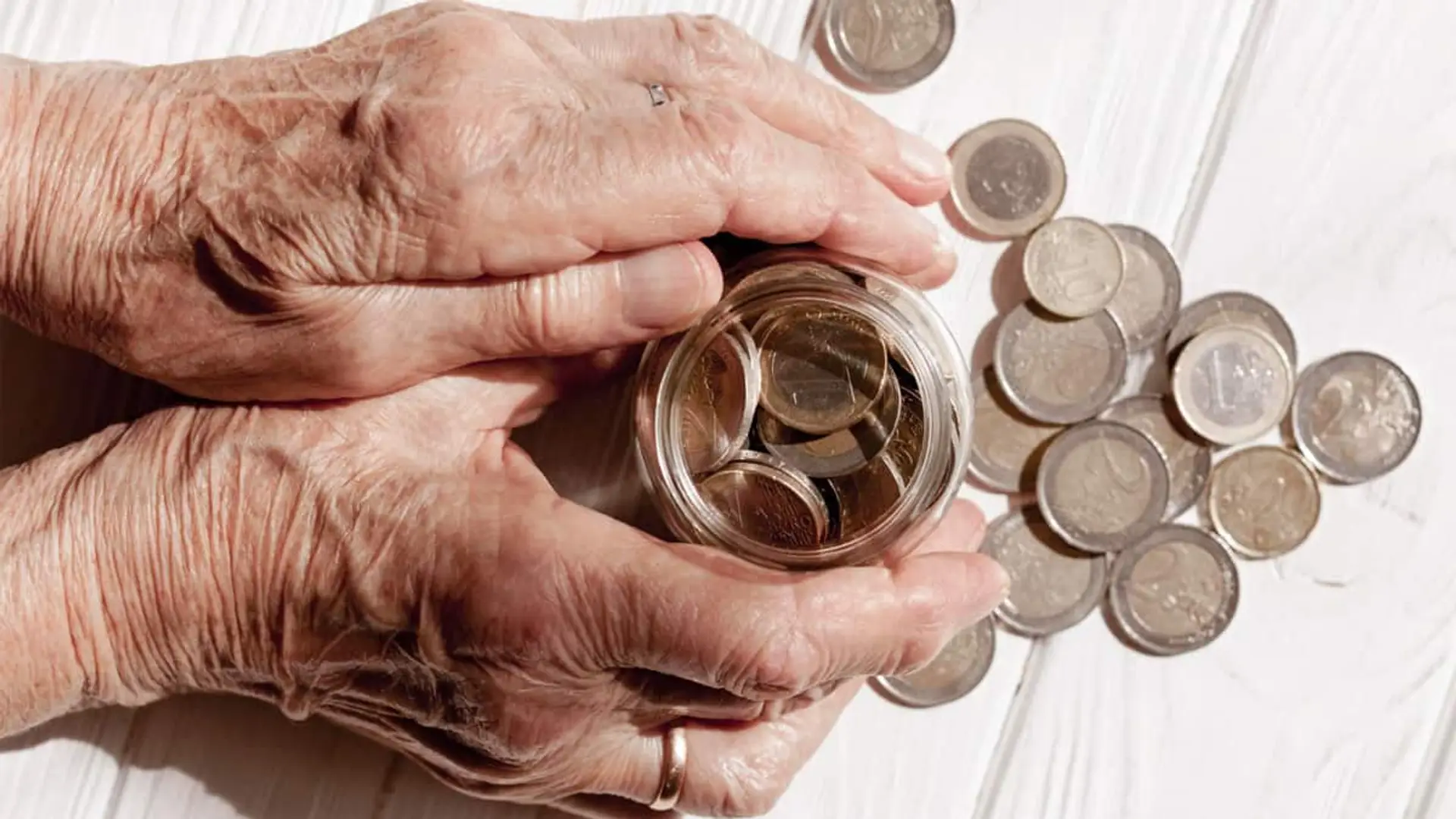 Manos de una persona mayor protegiendo un tarro con monedas de euro, símbolo del ahorro en la jubilación.