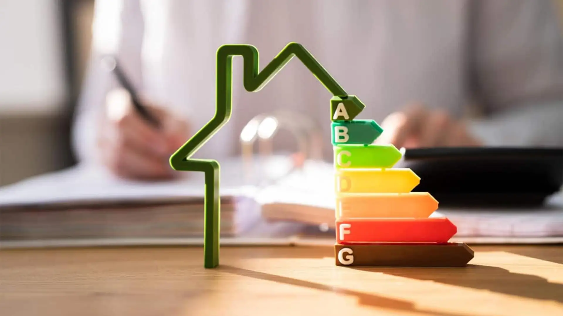 Cómo ahorrar en luz, revalorizar tu piso hasta un 8% y pagar menos en la Renta con una sola obra Maqueta de una casa junto a una escala de eficiencia energética de la A a la G sobre una mesa