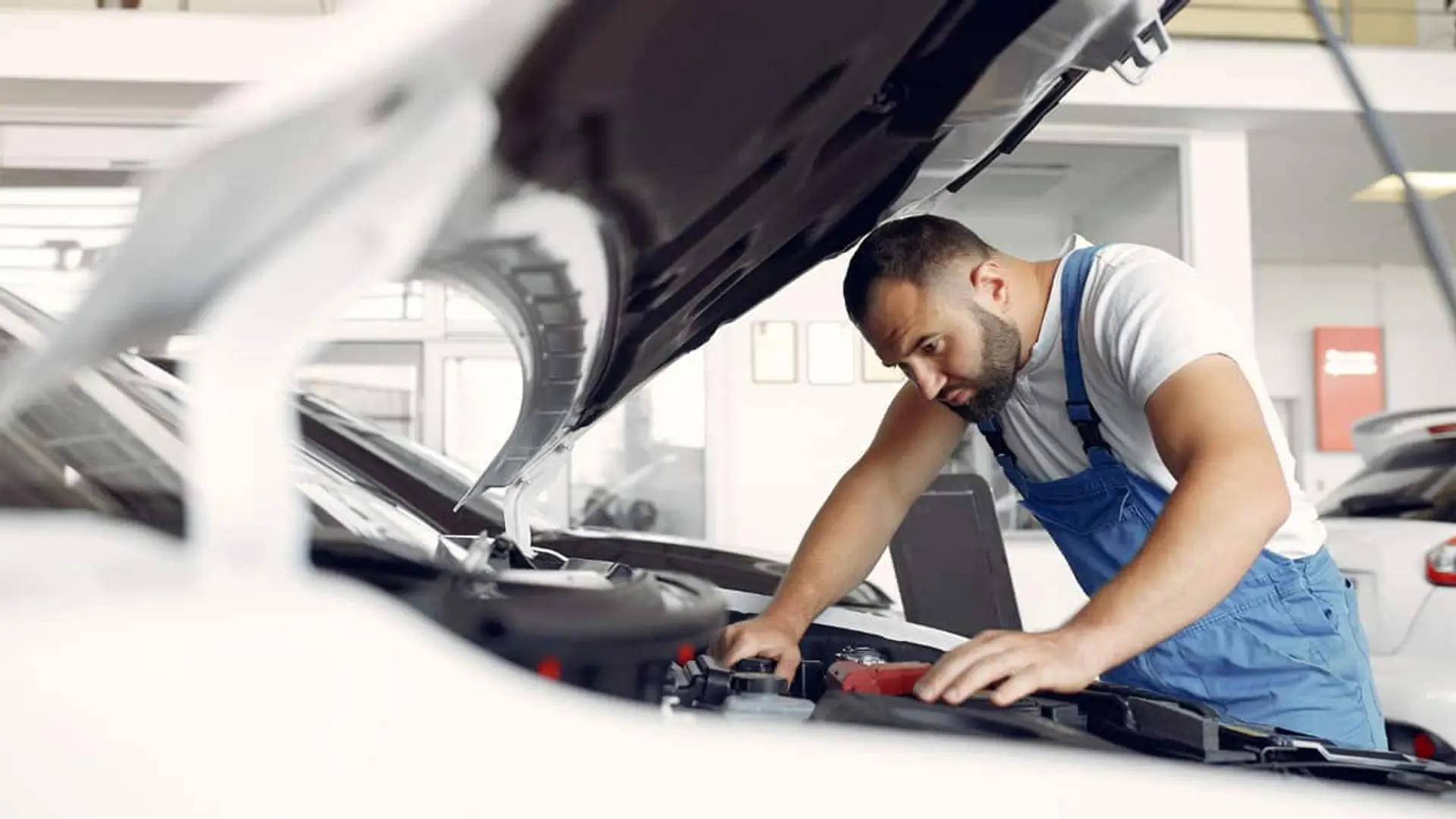 Mantener tu coche ya cuesta 4.254 euros al año: así se reparte cada euro Mecánico revisando el motor de un coche con el capó abierto