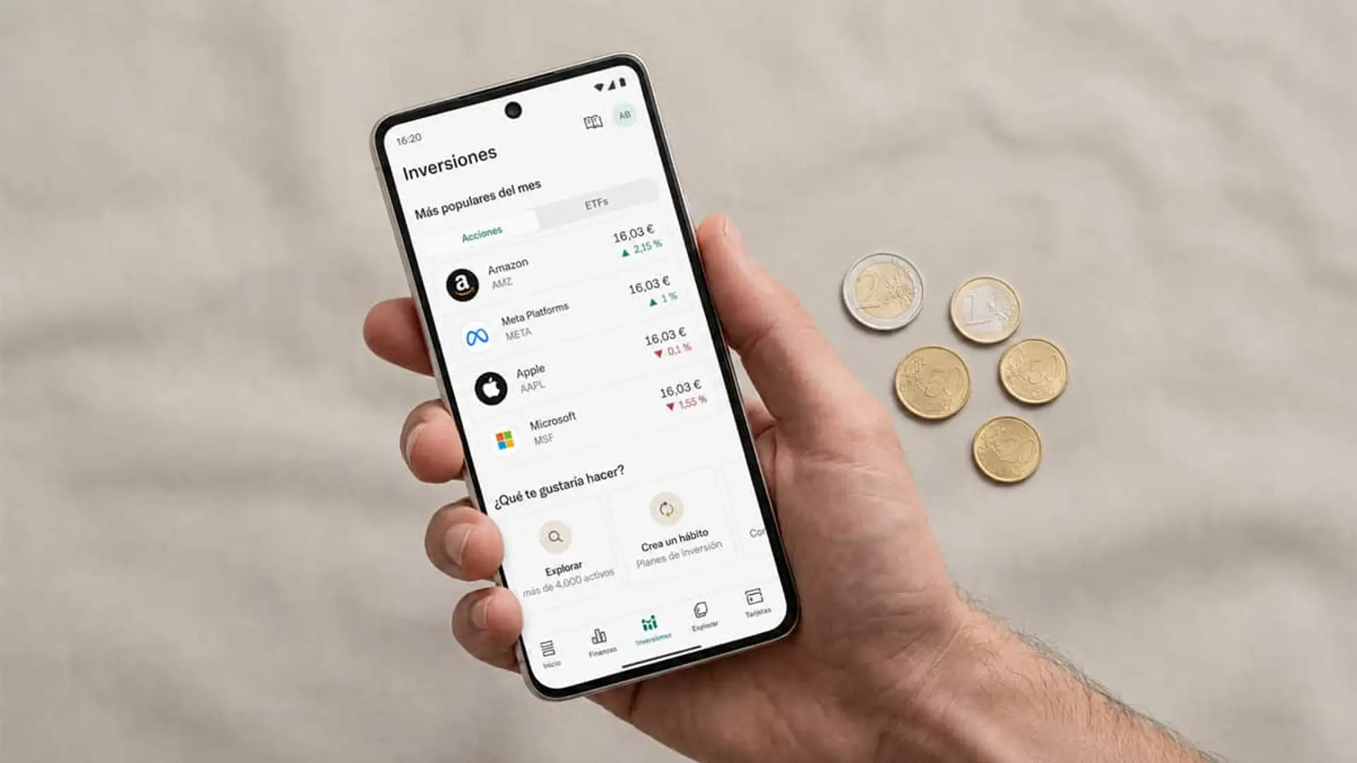 N26 acaba con año y medio de trading gratuito y vuelve a cobrar 0,90 euros por operación Mano sosteniendo un móvil con app de N26 con inversiones en acciones y varias monedas de euro sobre la mesa.