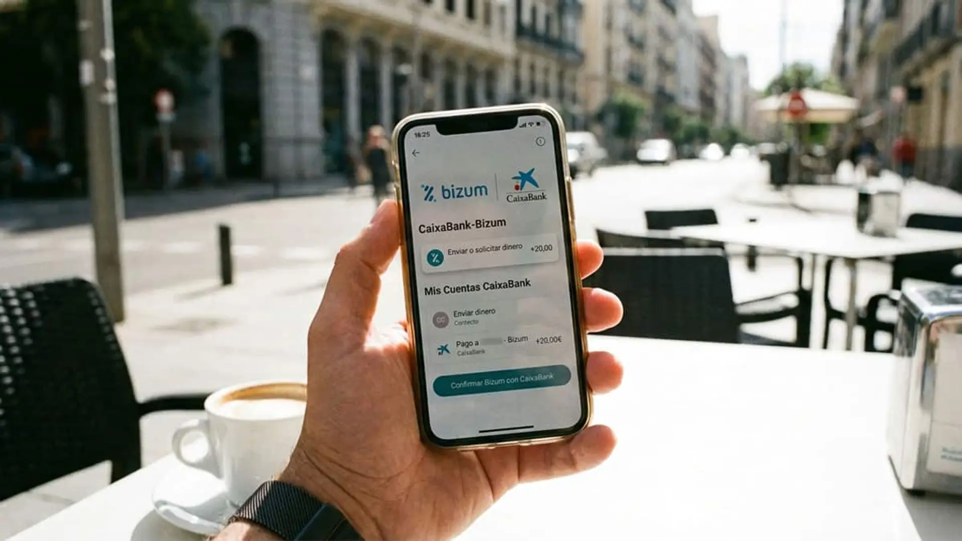 Mano sosteniendo un móvil con Bizum y CaixaBank en la pantalla sobre una mesa de terraza
