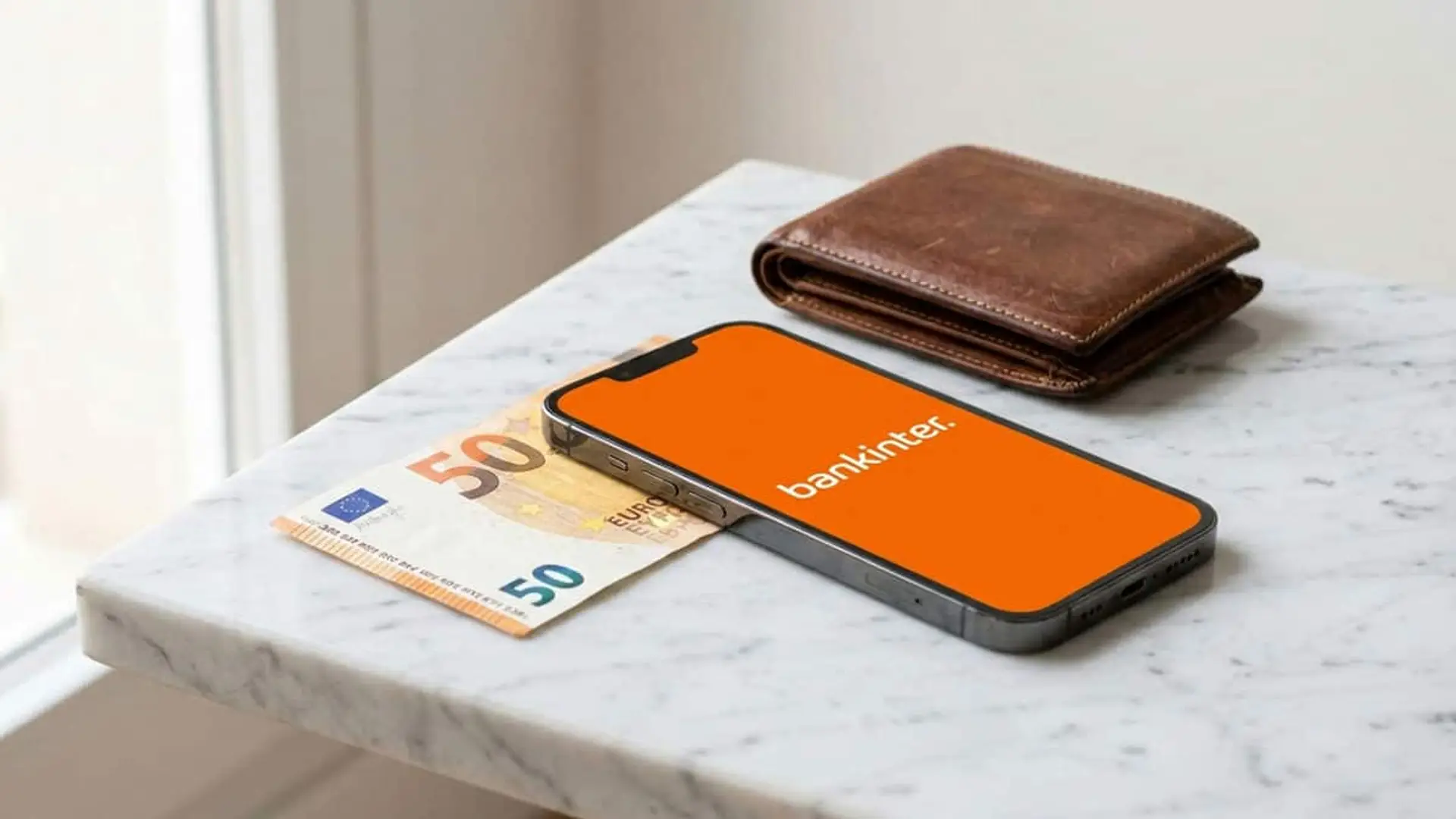 Móvil con el logotipo de Bankinter junto a una billetera y un billete de 50 euros sobre una superficie de mármo