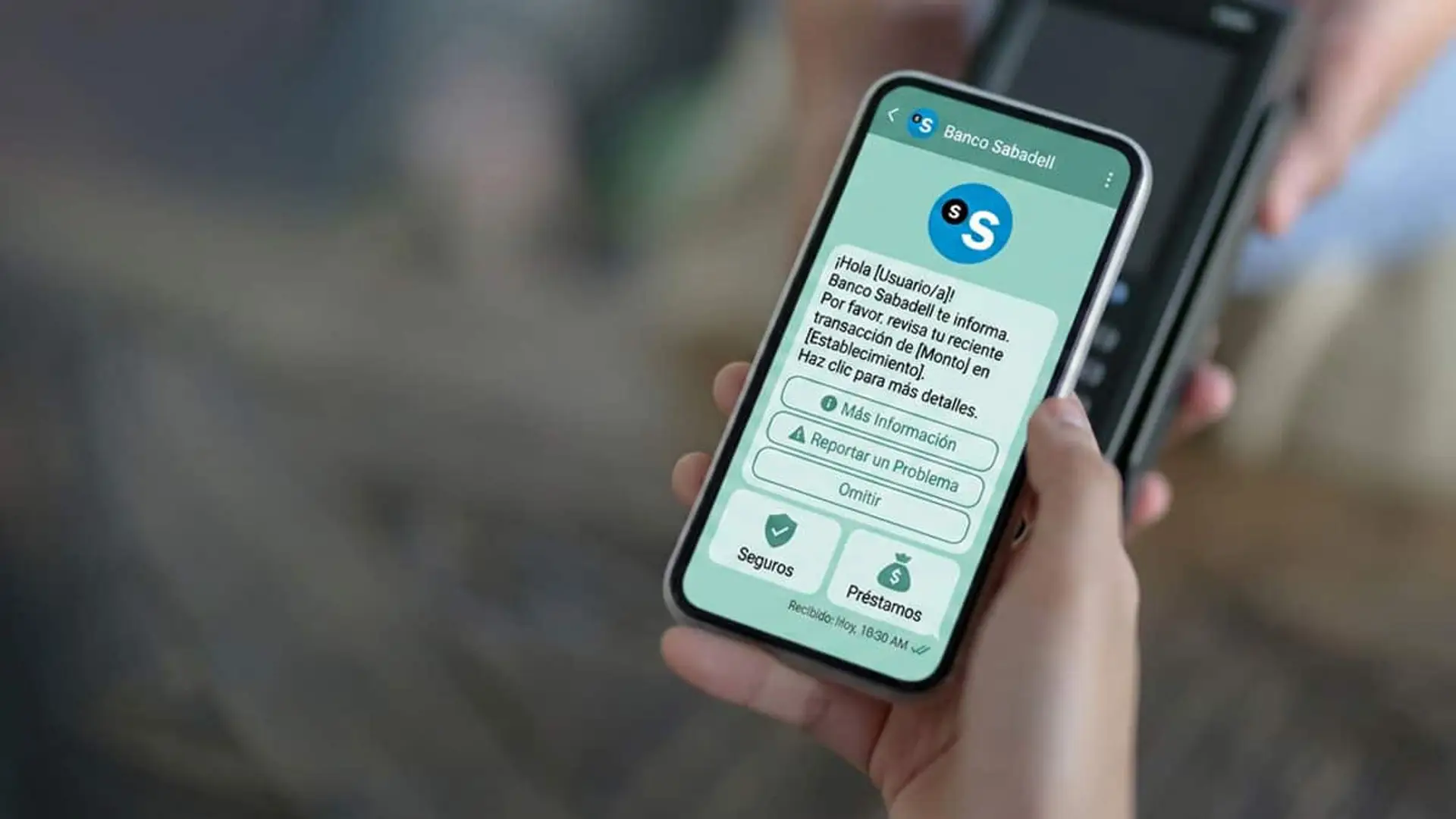Mano sosteniendo un móvil con un mensaje de Banco Sabadell en la pantalla