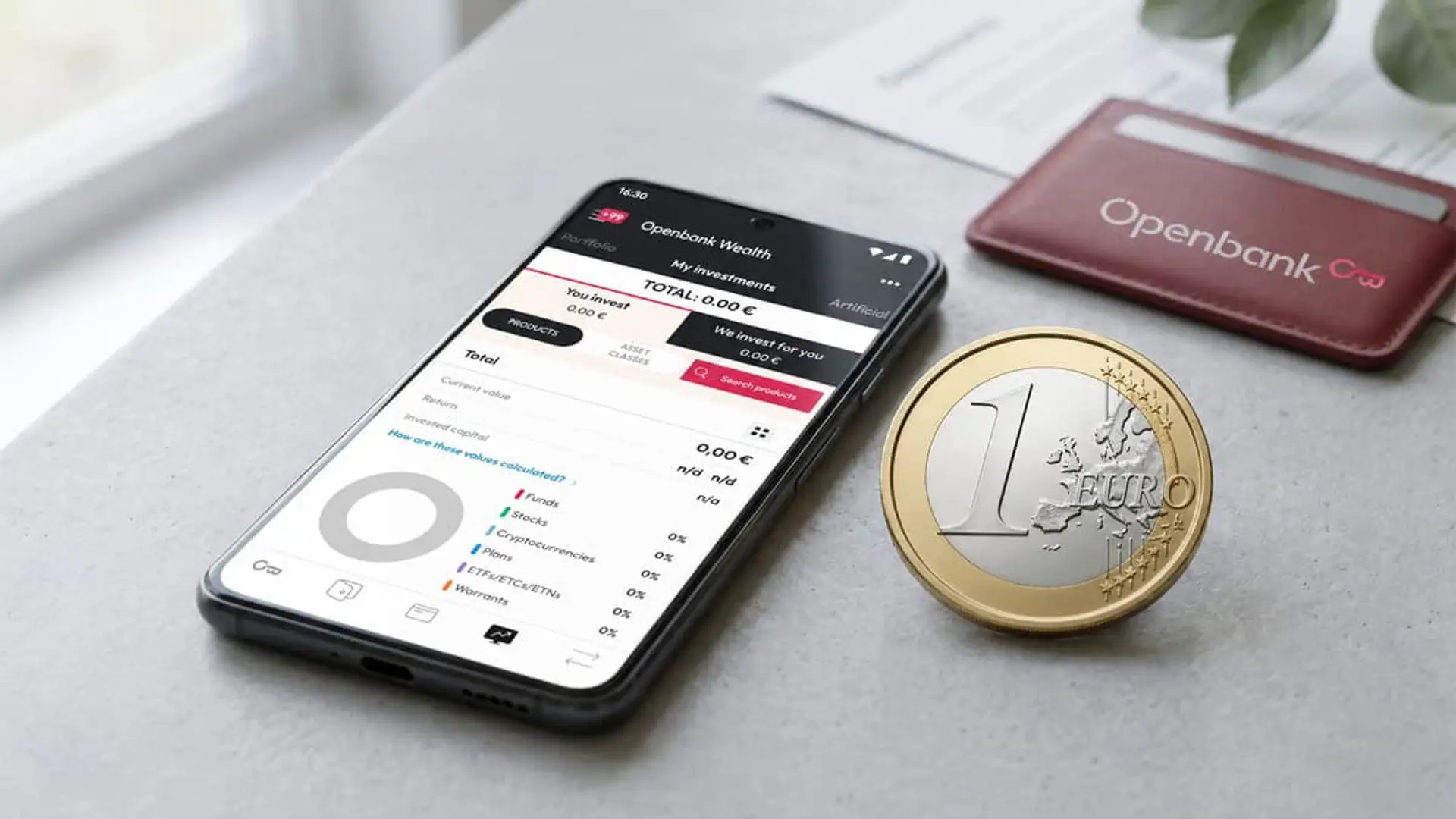 Móvil con la plataforma de inversión de Openbank junto a una moneda de euro y una cartera de Openbank