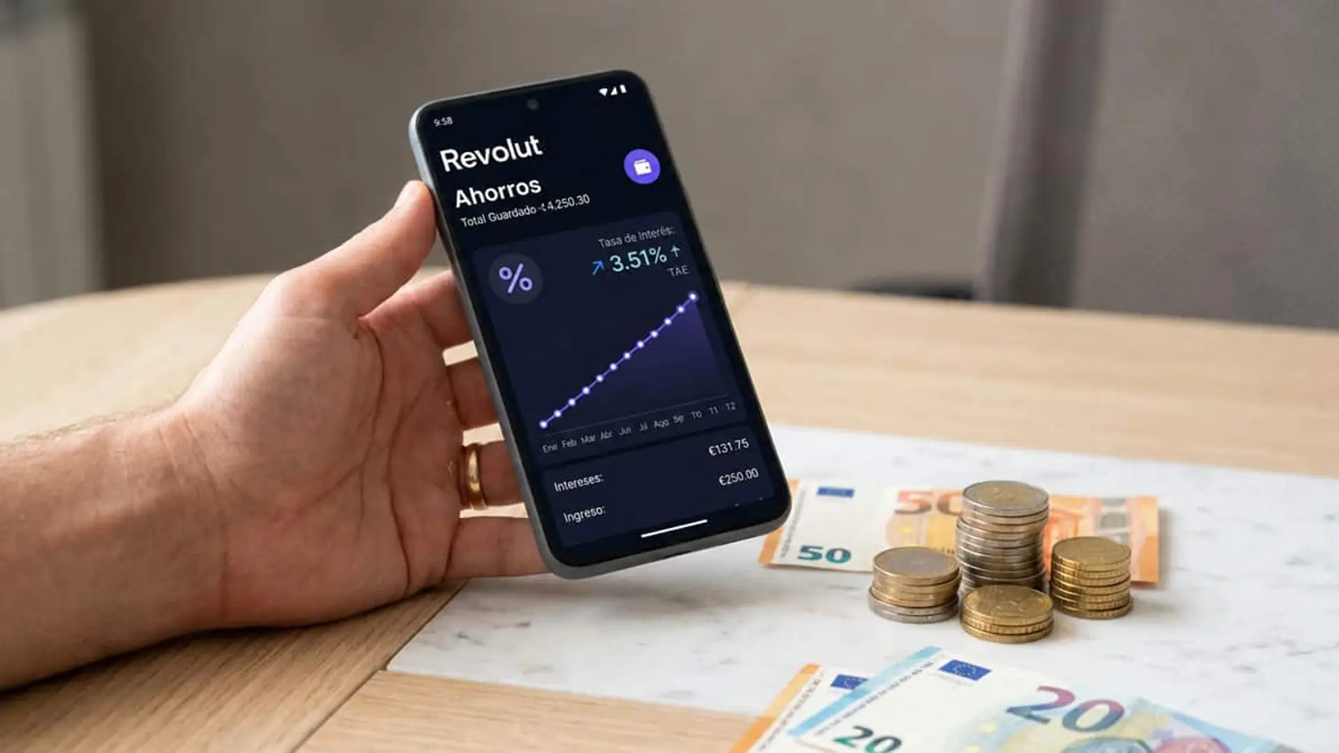 La cuenta de Revolut al 3,51% TAE rinde más que la banca, pero solo hasta 25.000 euros y 4 meses Mano sosteniendo un móvil con la sección de ahorros de Revolut junto a monedas y billetes de euro