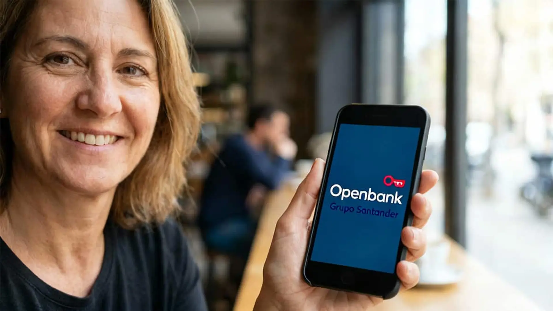 Mujer mostrando la app de Openbank en su móvil dentro de una cafetería.