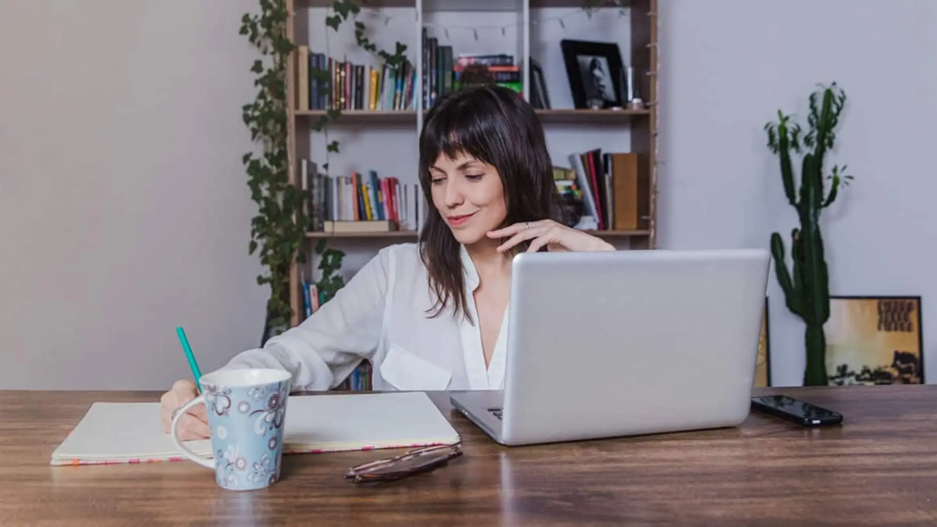 La justicia frena a Hacienda: los autónomos que trabajan desde casa podrán deducirse más gastos de luz, agua e internet Mujer trabajando desde casa con un portátil, tomando notas en un escritorio