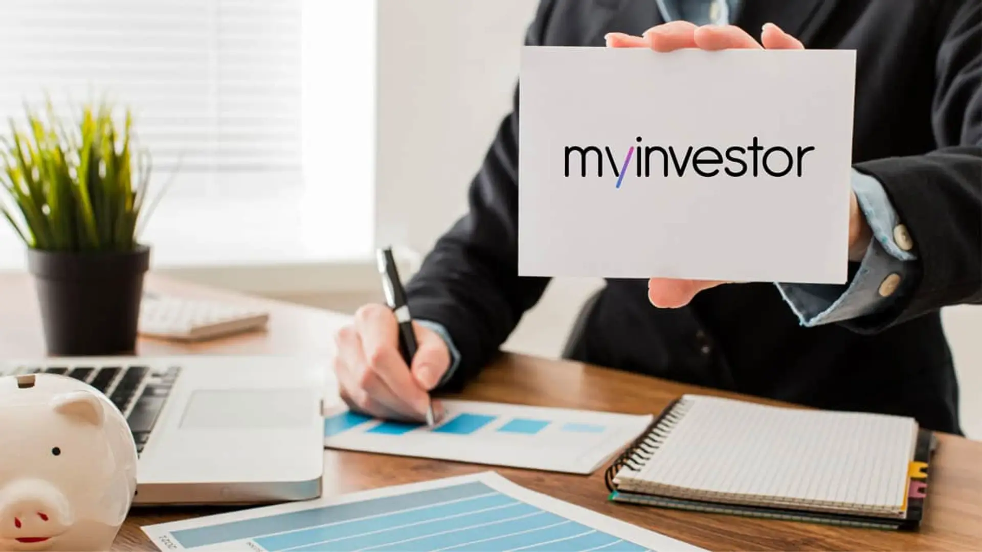 Asesor de MyInvestor con hucha y gráficos bursátiles para la gestión de inversiones y cuentas de ahorro.