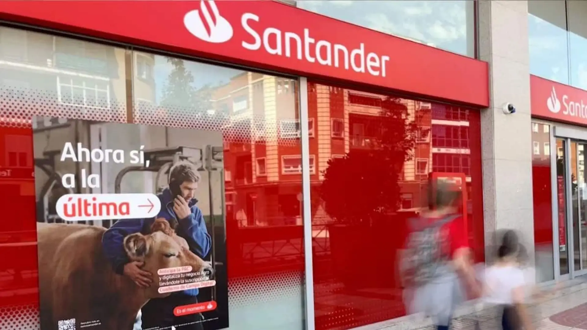 Fachada de una oficina del Banco Santander con un cartel publicitario en el escaparate.