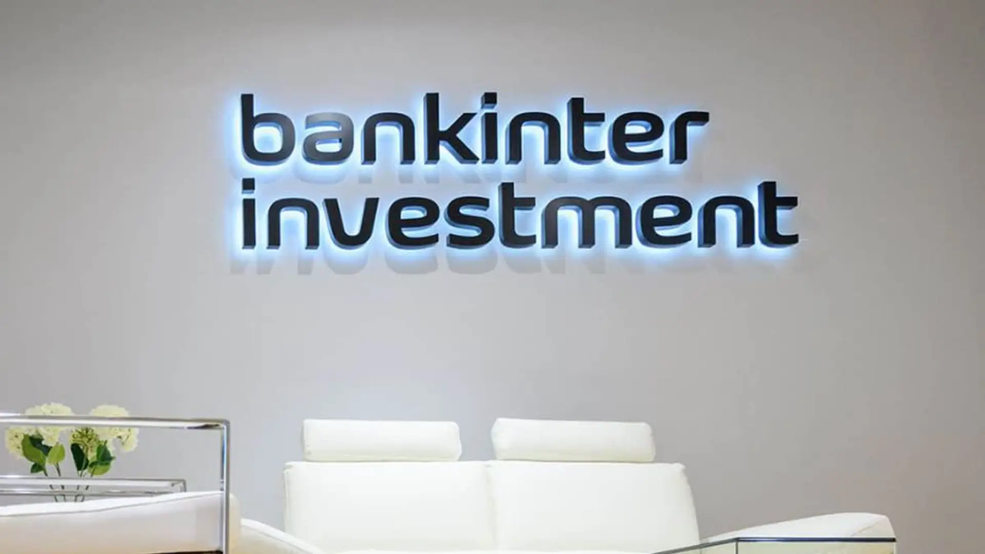 Logotipo de Bankinter Investment retroiluminado en la pared de una oficina moderna con mobiliario blanco.