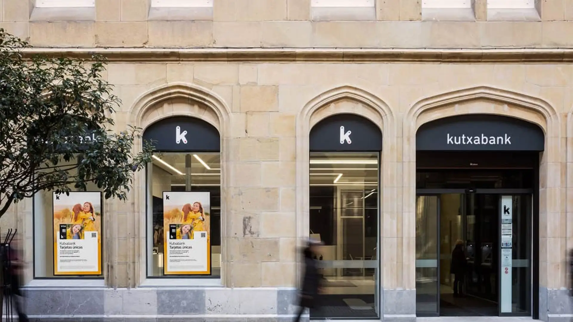 Fachada exterior de una oficina bancaria de Kutxabank con su logotipo oficial y carteles promocionales.
