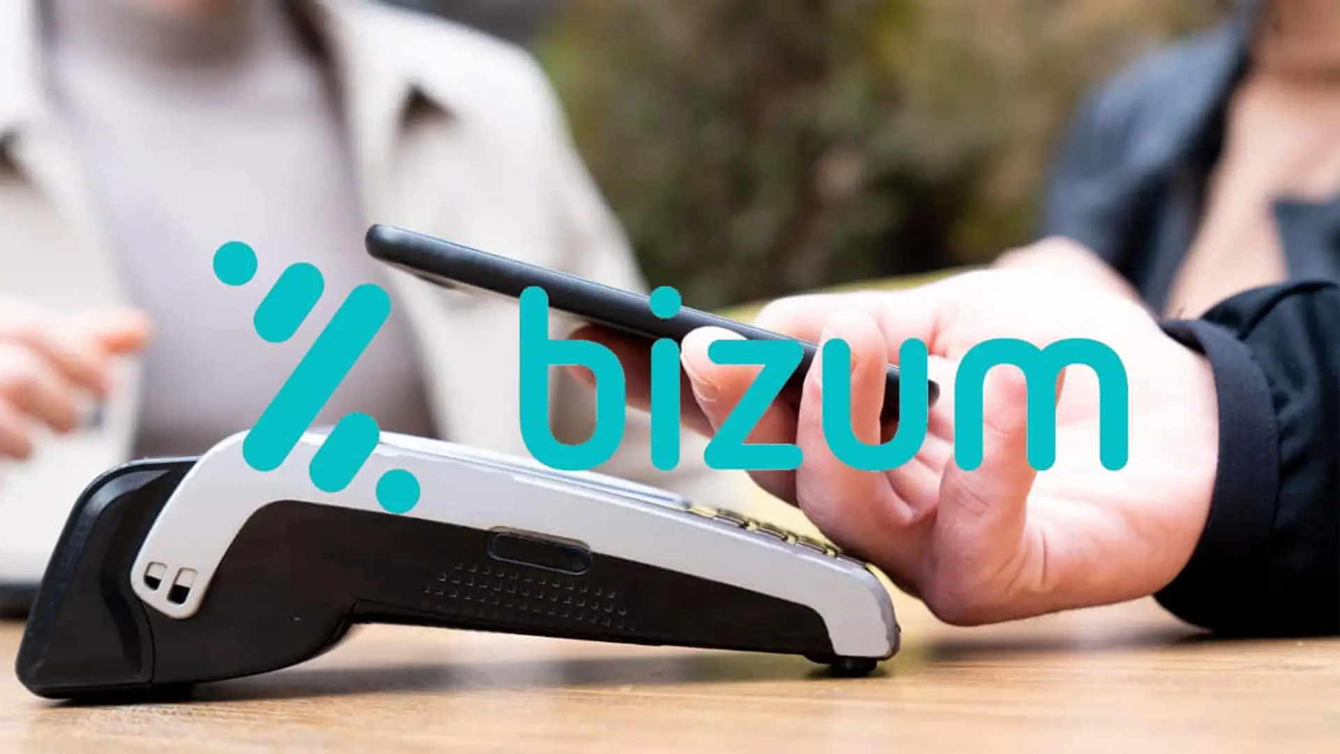 Persona acercando un móvil a un terminal de pago con el logotipo de Bizum sobre la imagen